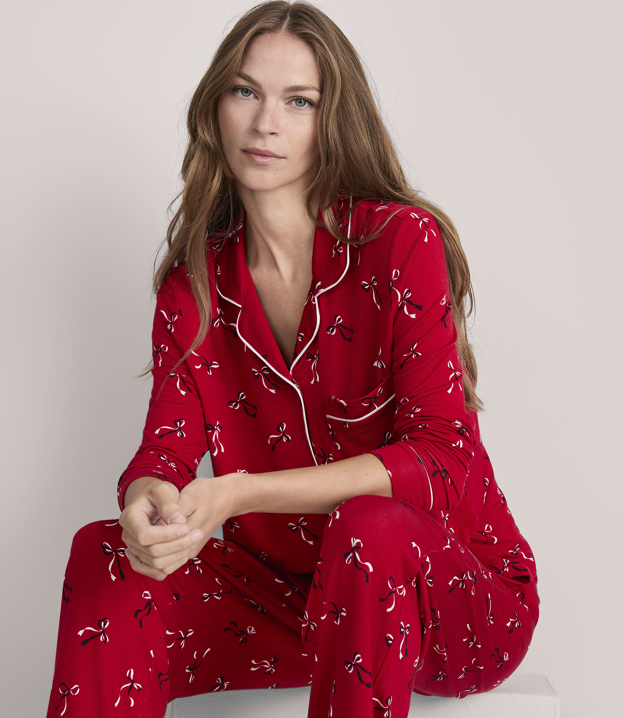 A woman in red pajamas with a bow pattern sits against a plain gray background.