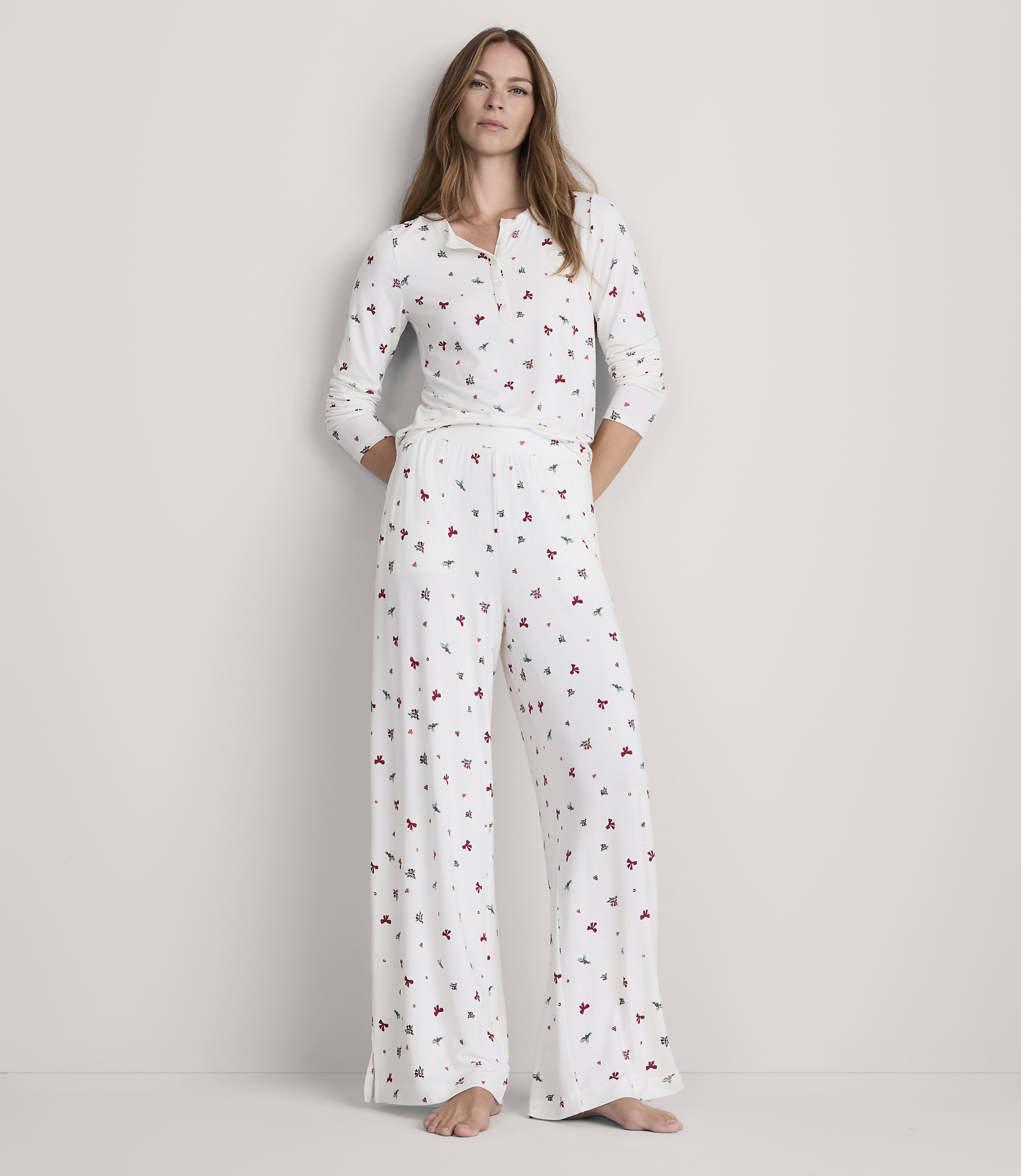 A woman stands in a white pajama set with a subtle heart pattern, against a plain, light-colored background.