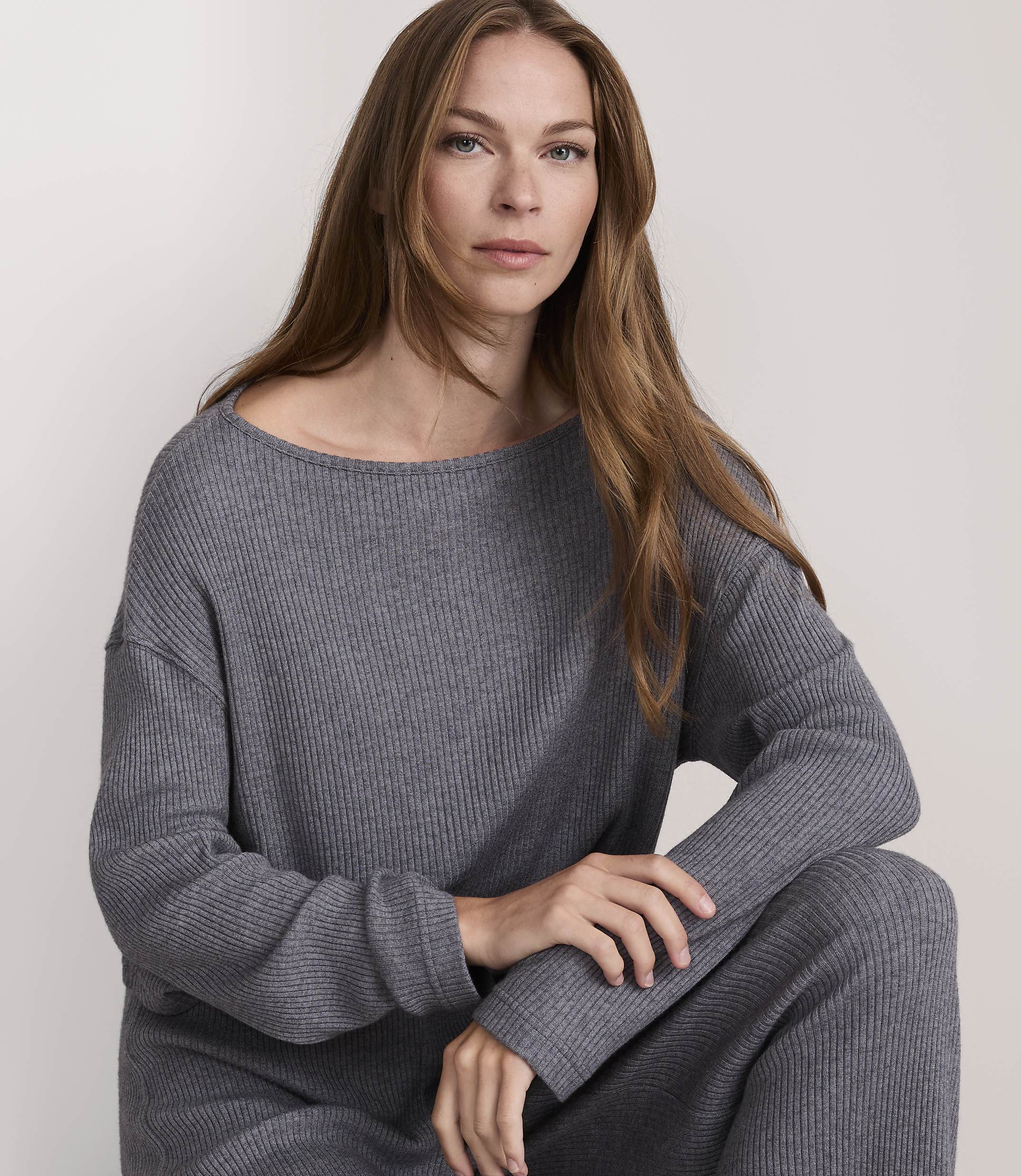 A woman in a grey ribbed sweater and pants poses against a plain, light background.