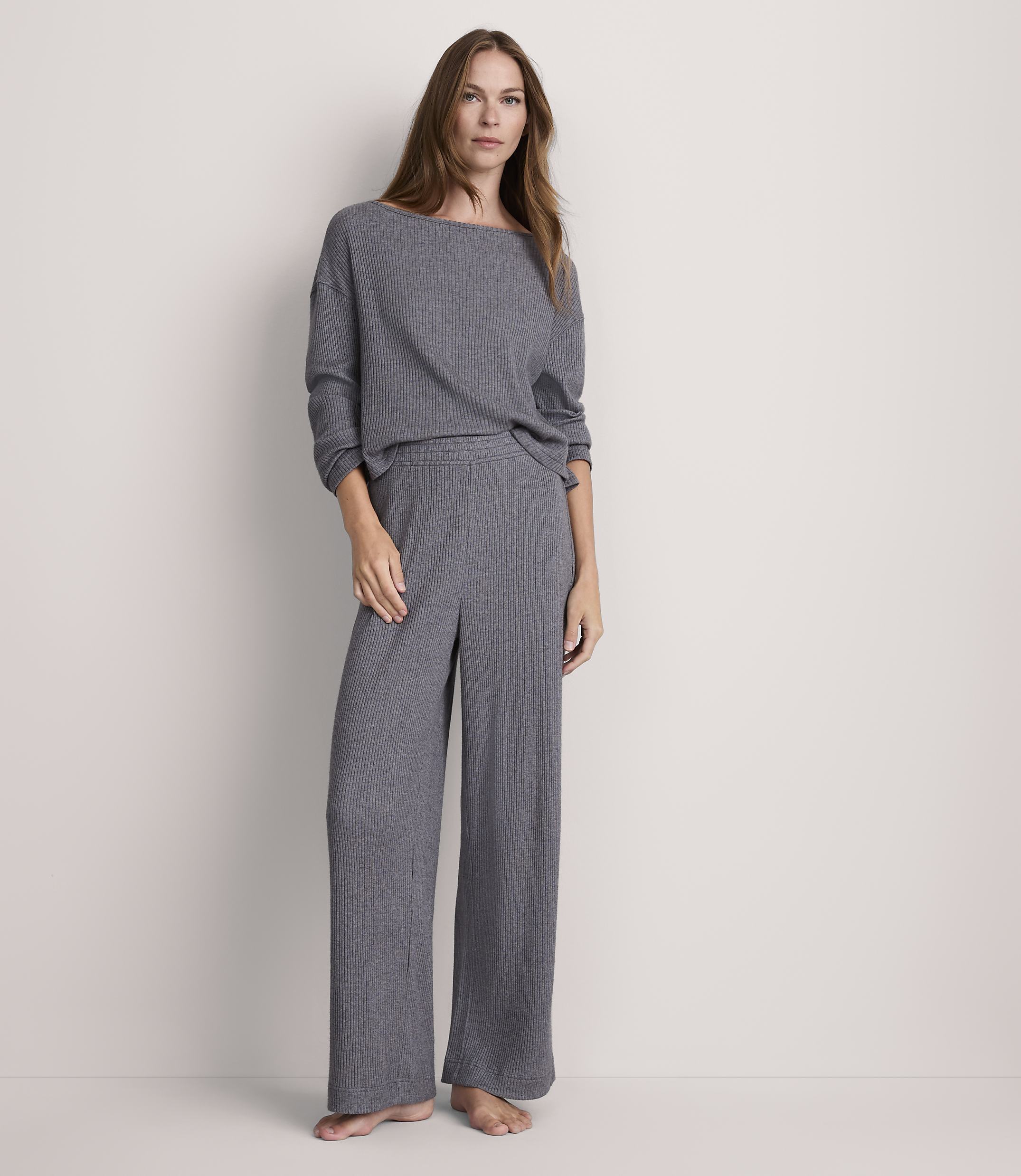 A woman stands in a grey ribbed loungewear set against a plain, light grey background.