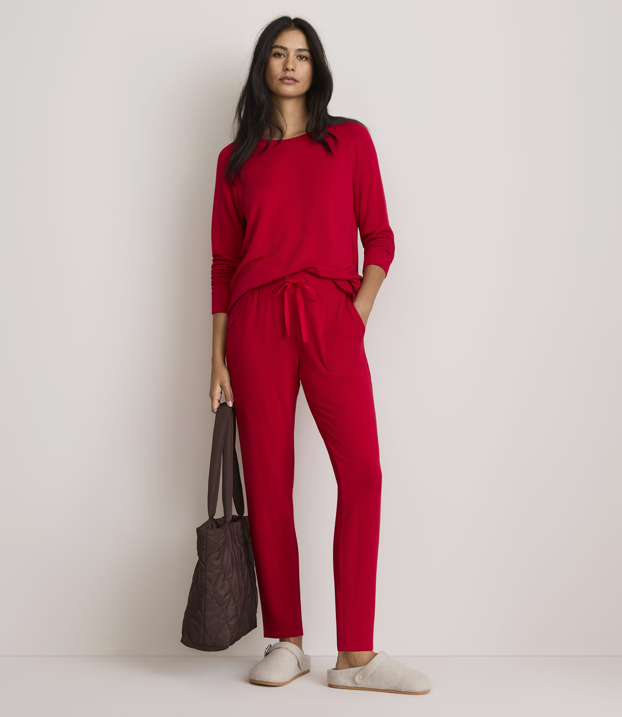 A woman in red pajamas stands with a brown tote bag and slippers against a plain white background.