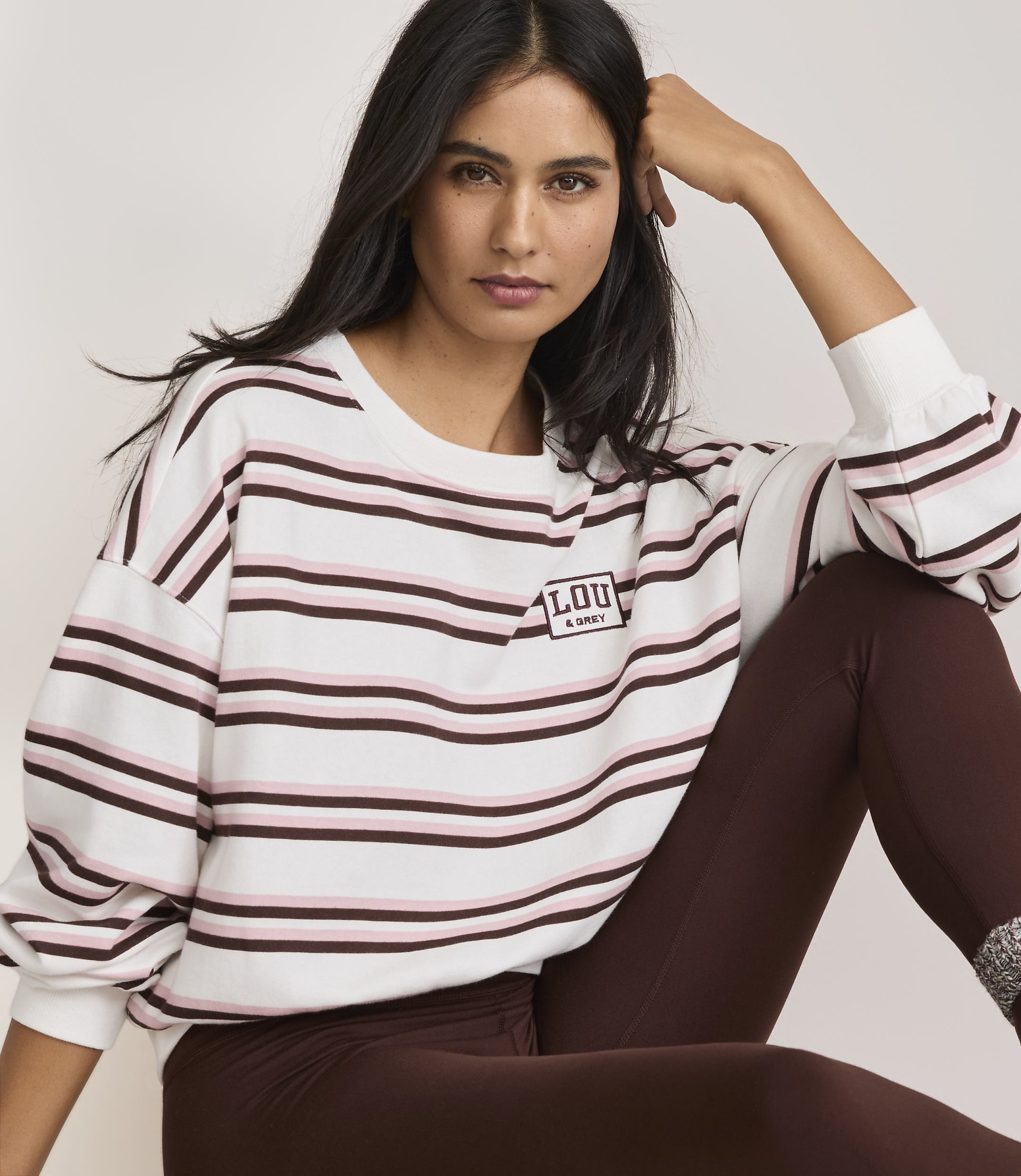 A woman in a striped sweatshirt and brown leggings poses against a plain background.