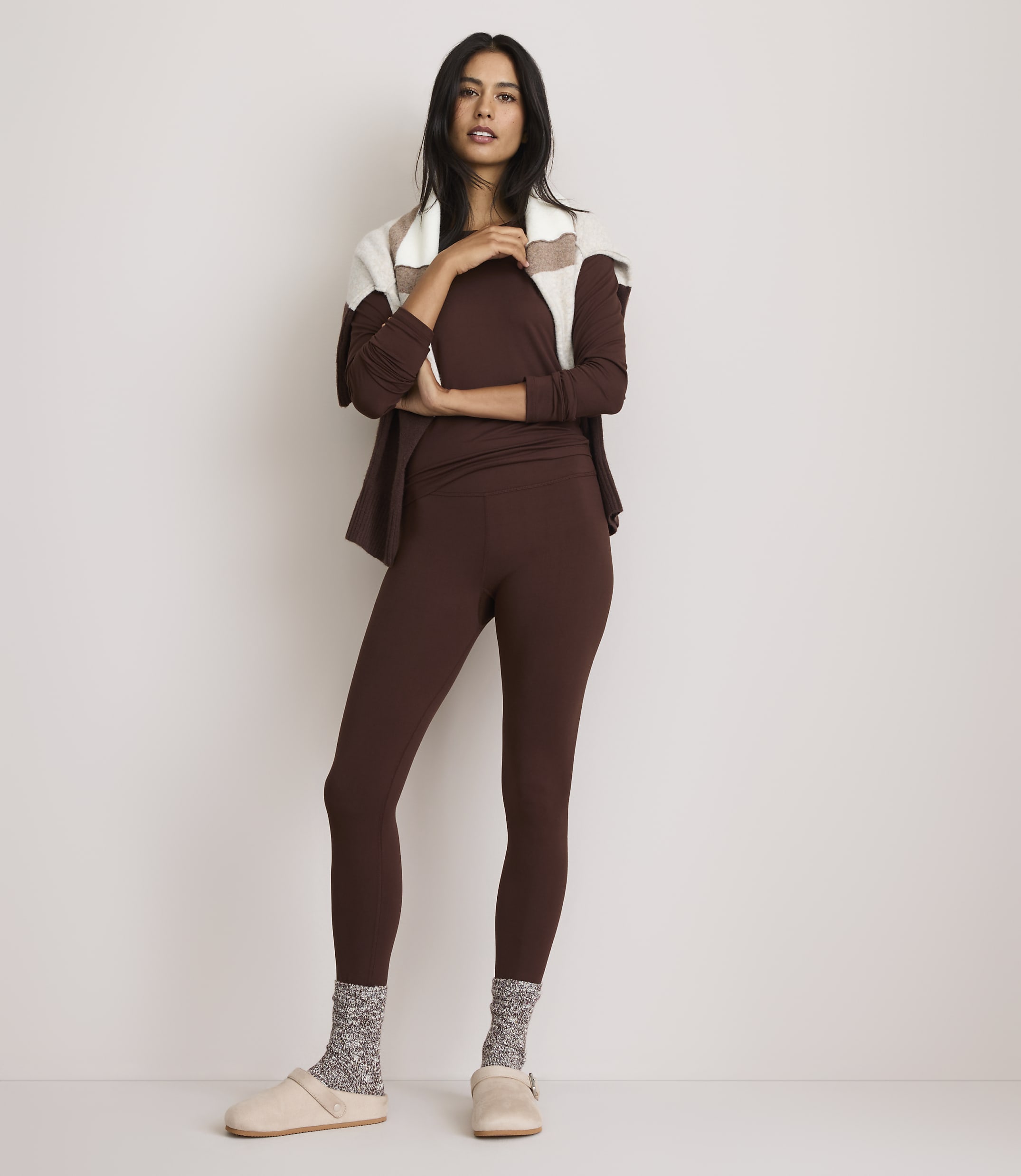 A woman in brown loungewear and patterned socks stands against a plain white background.