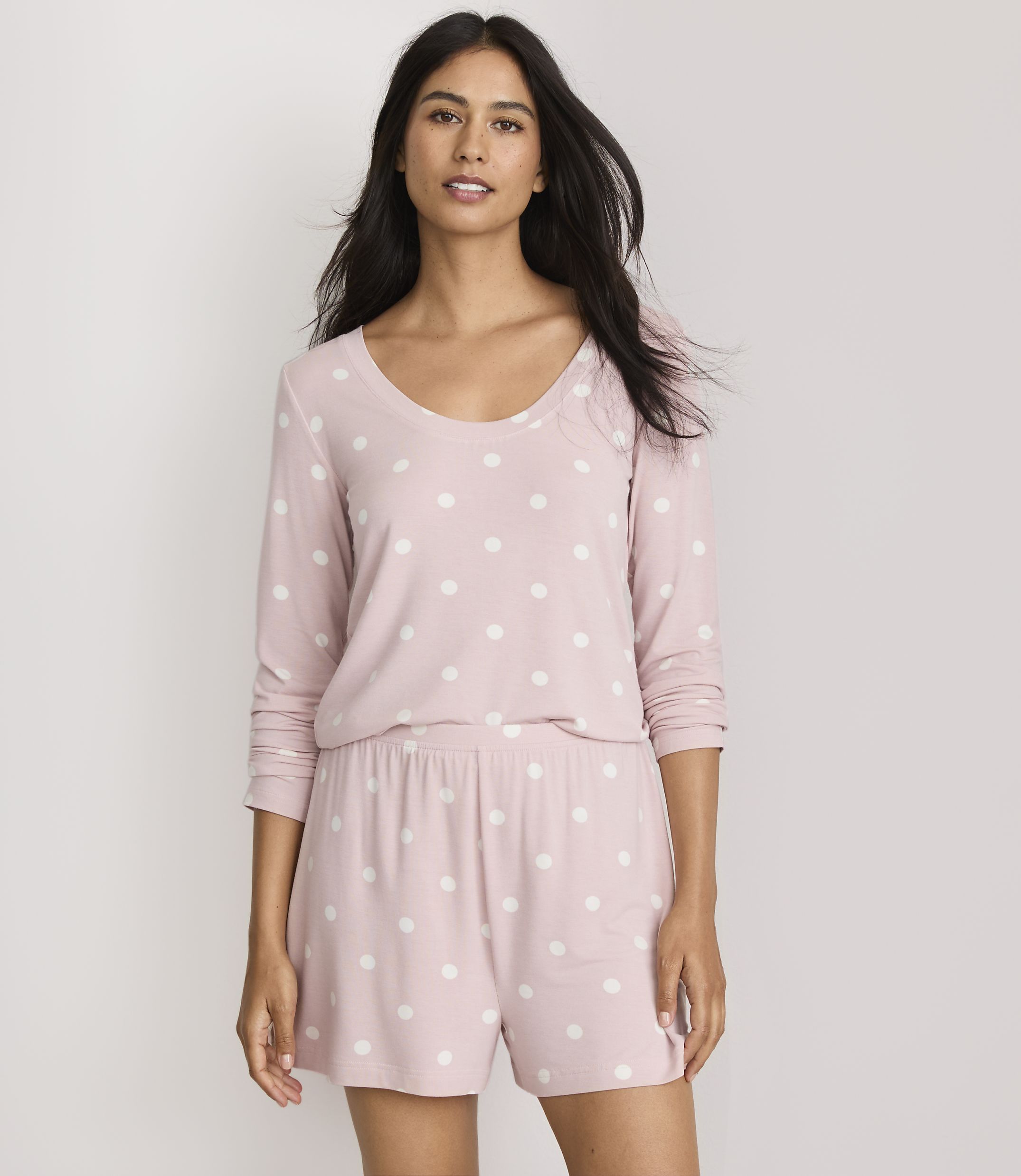 A woman in a pink polka dot pajama set stands against a plain white background.