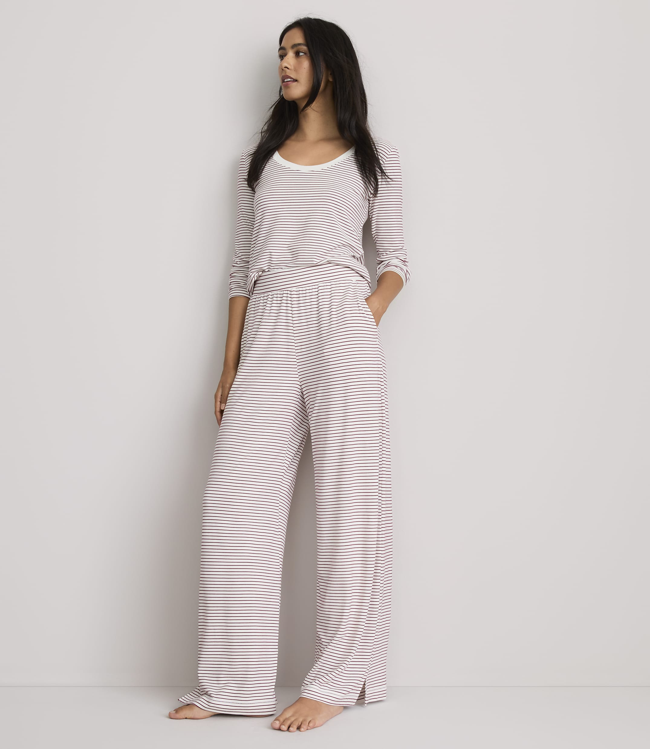 A woman in striped pajamas stands against a plain, light-colored wall.