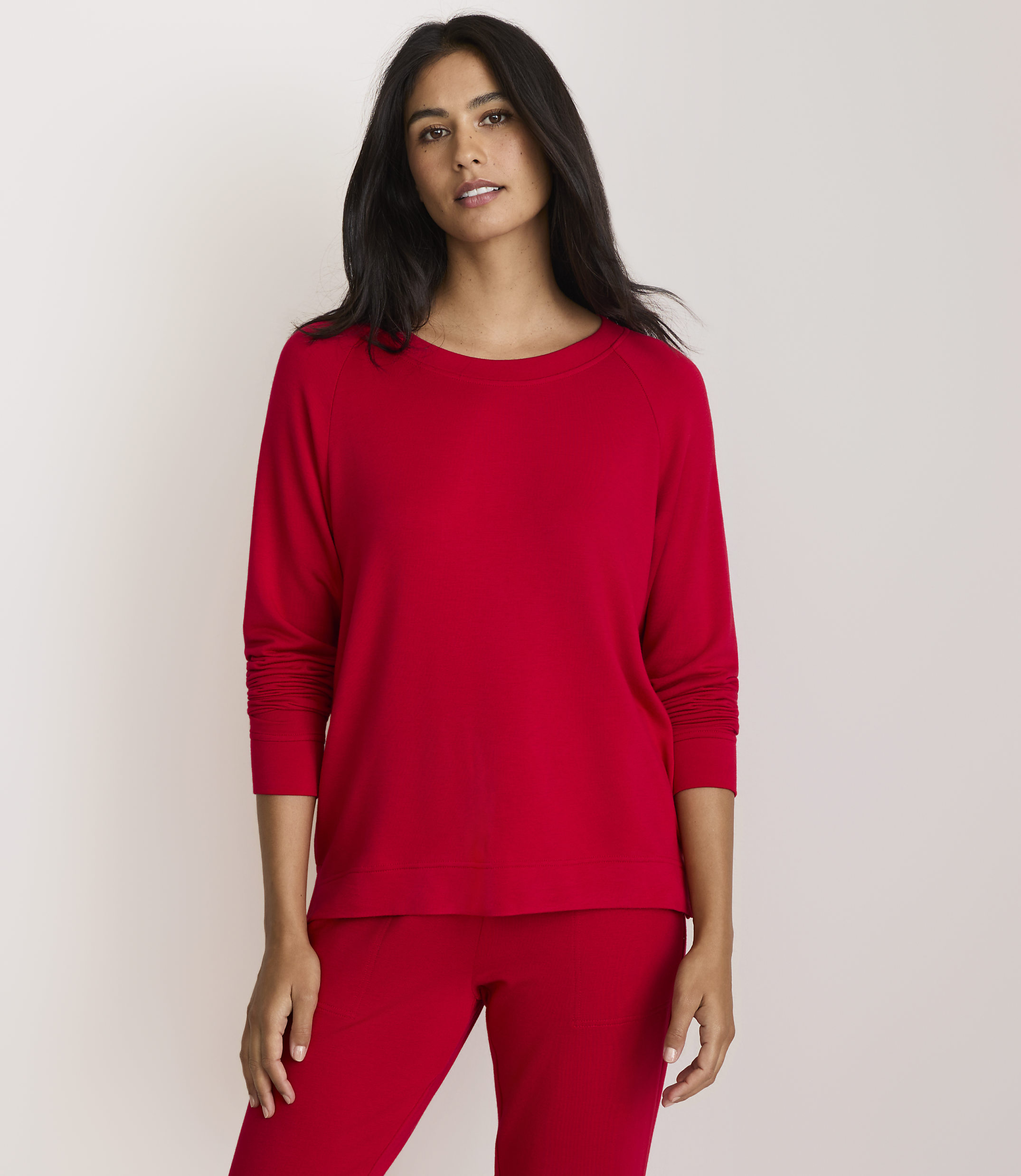 A woman in a red top and pants stands against a plain white background.
