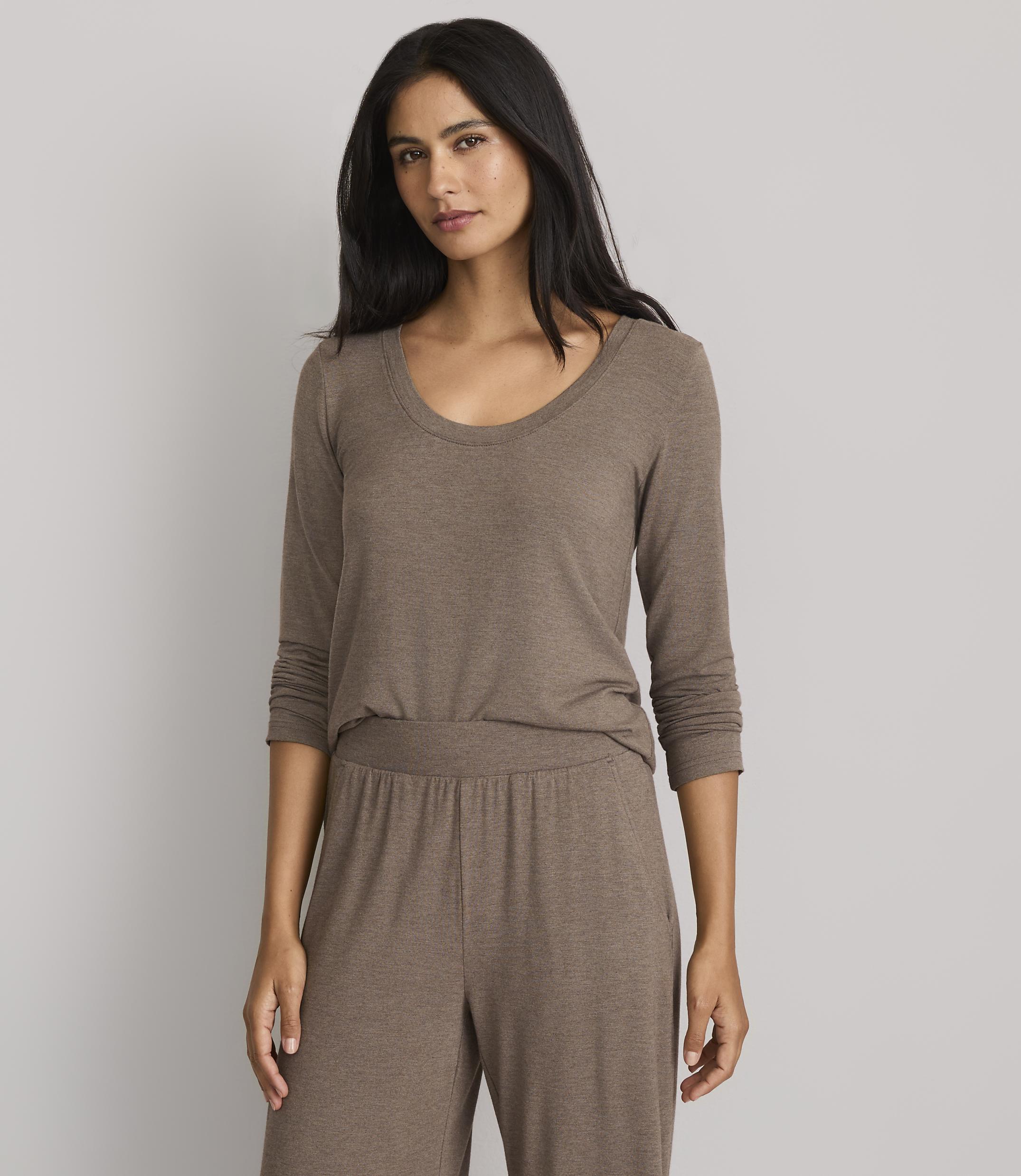 A woman in a brown long-sleeved shirt and matching pants stands against a plain gray background.