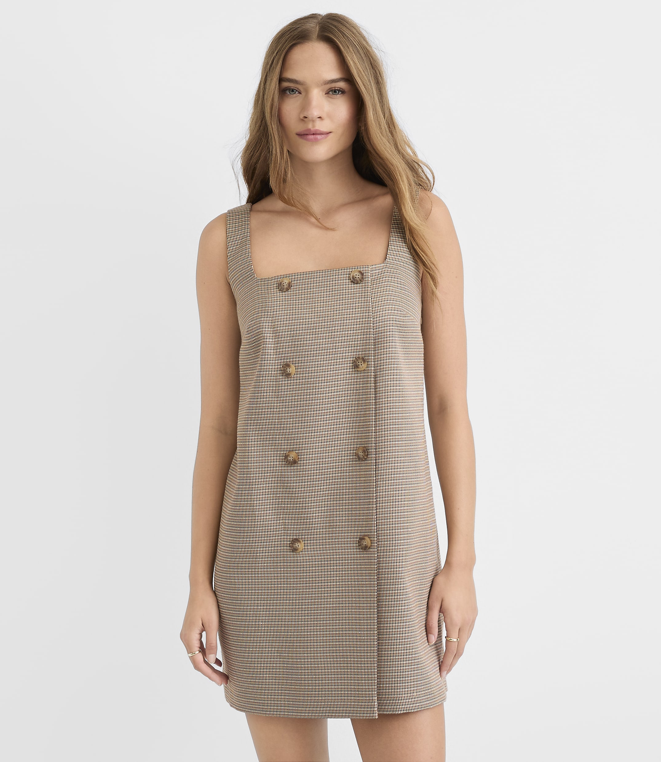 A young woman in a plaid dress stands against a plain white background.