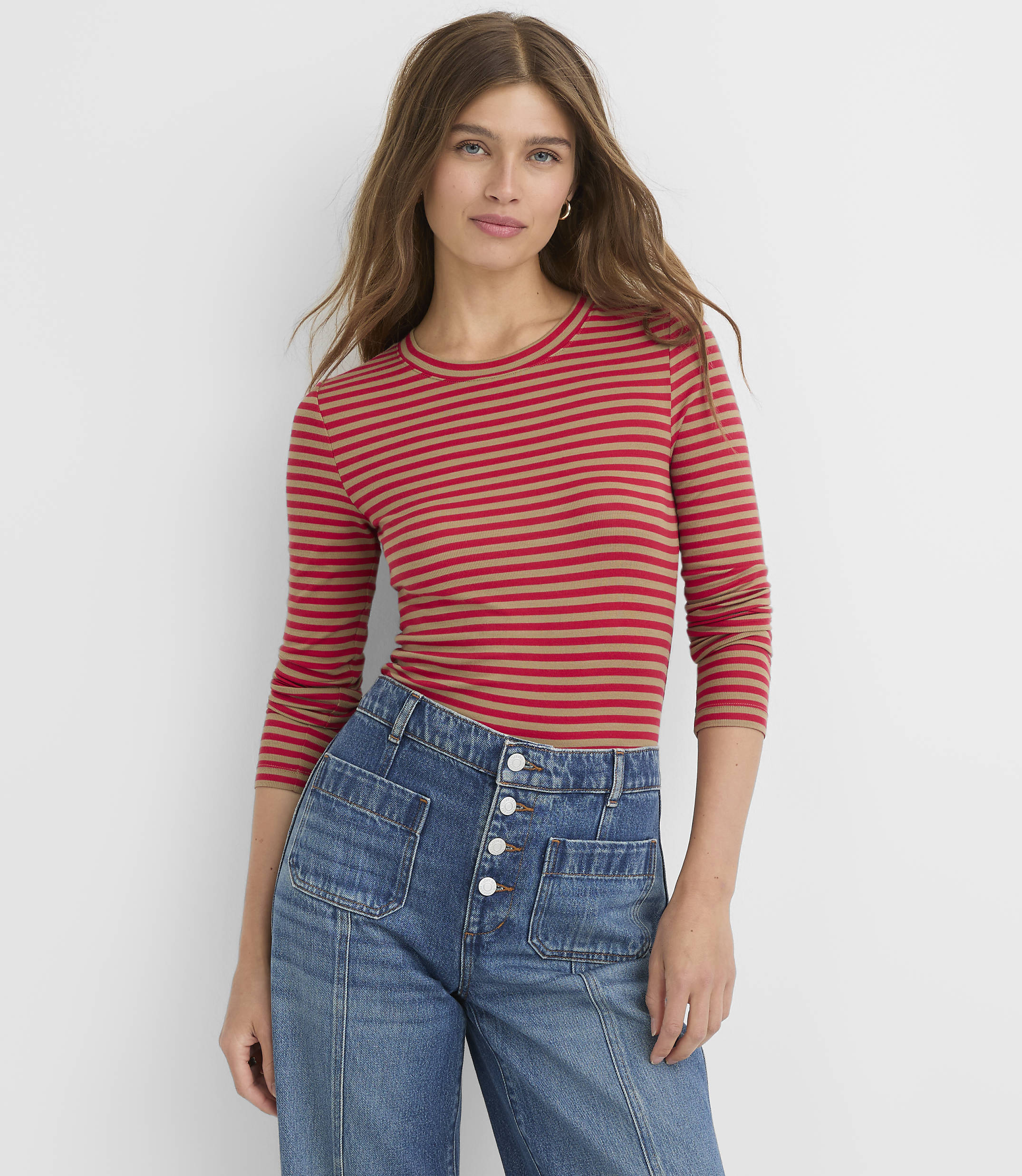 A woman in a red striped shirt and blue jeans stands against a plain white background.