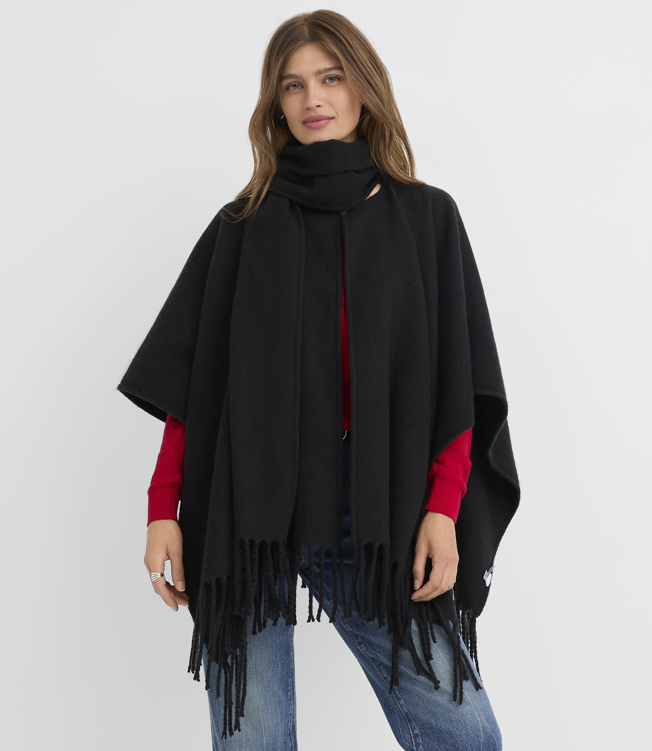 A woman in a black fringed poncho and scarf stands against a plain white background.