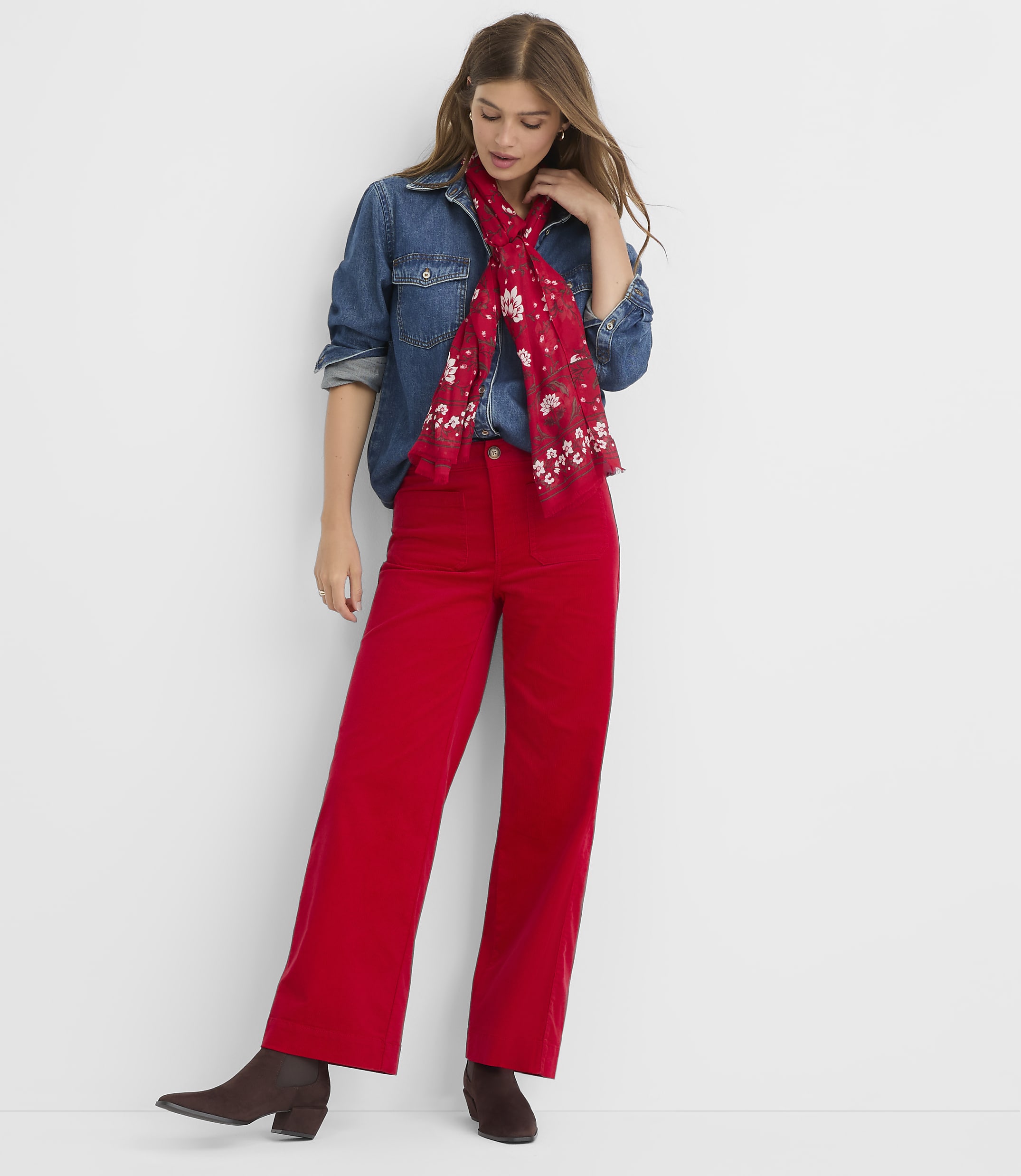 A woman in a denim shirt, red scarf, and red wide-leg pants stands against a plain white background.