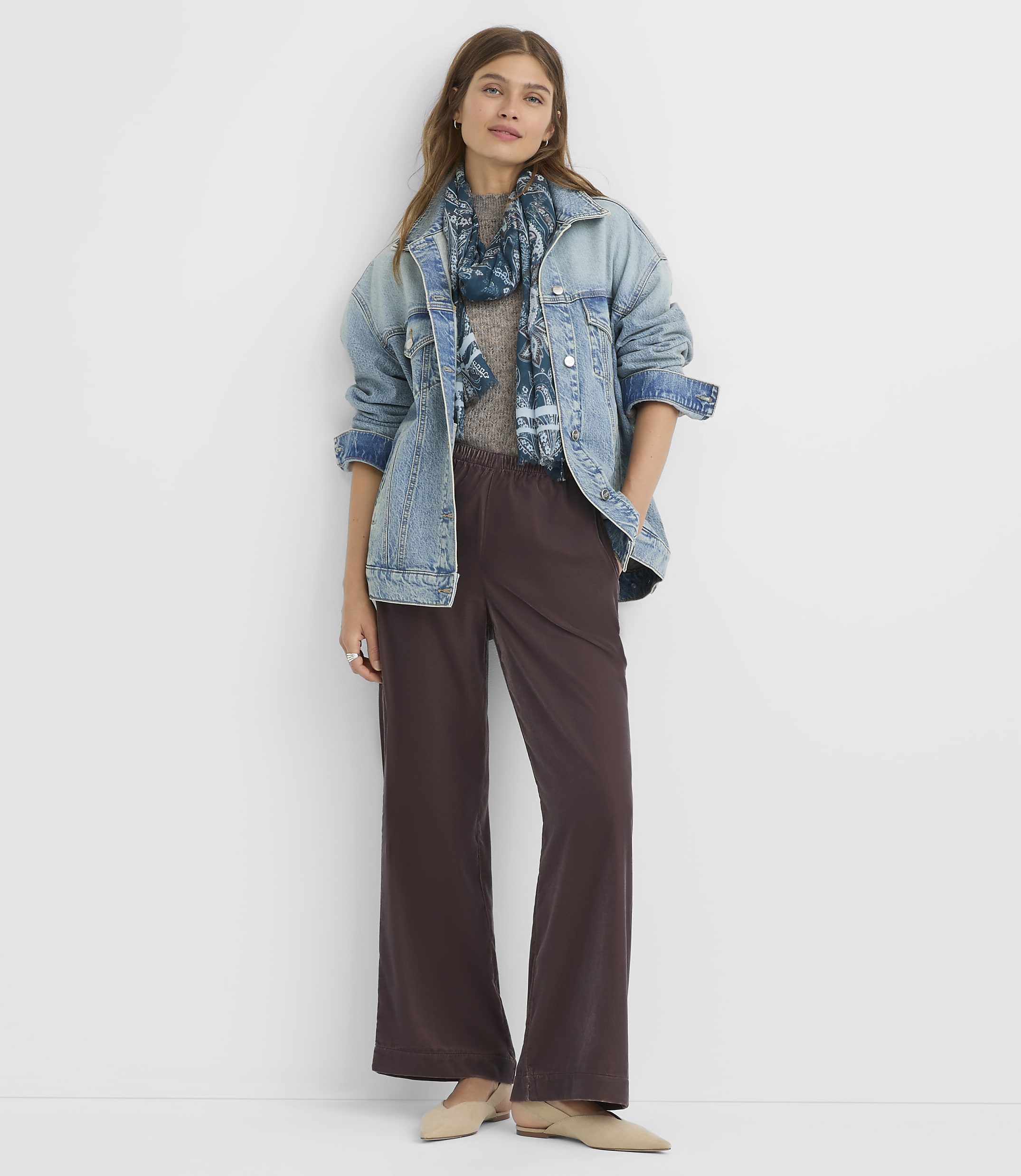 A woman in a denim jacket and wide-leg pants stands against a plain white background.