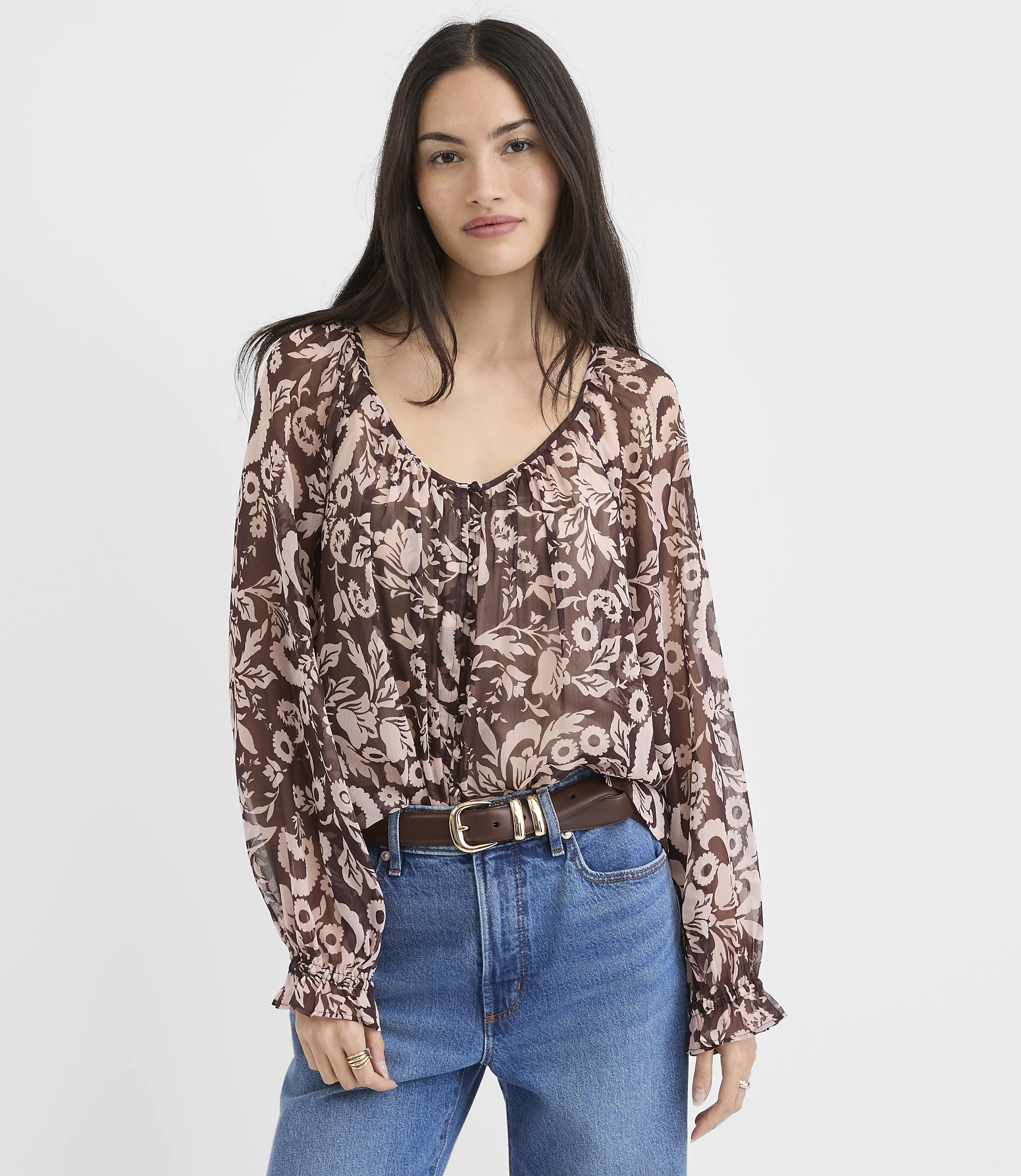 A woman in a floral print blouse and jeans stands against a plain white background.
