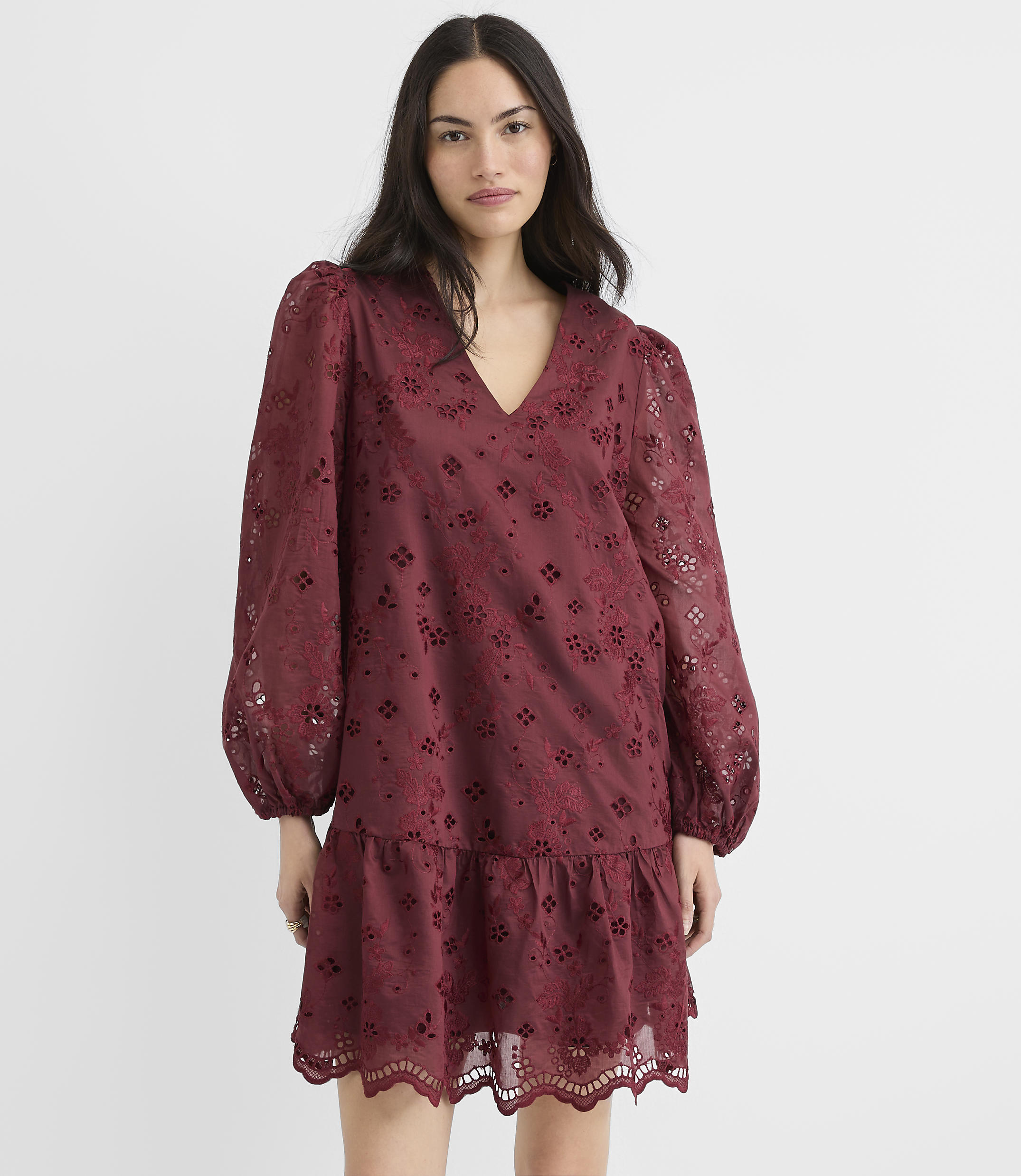 A woman in a burgundy eyelet dress with voluminous sleeves stands against a plain white background.