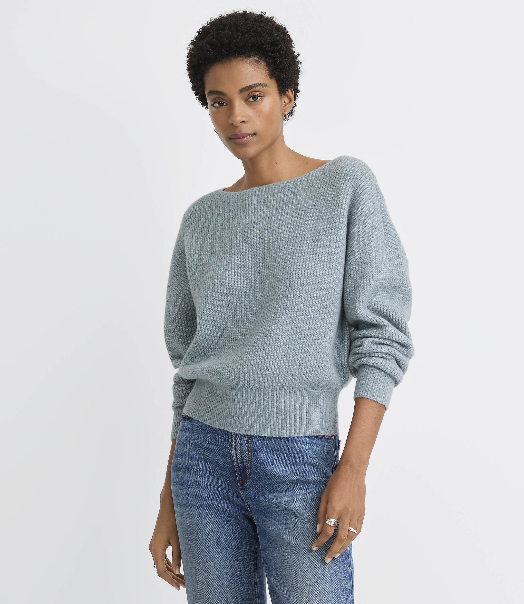 A woman in a light blue sweater and jeans stands against a plain white background.