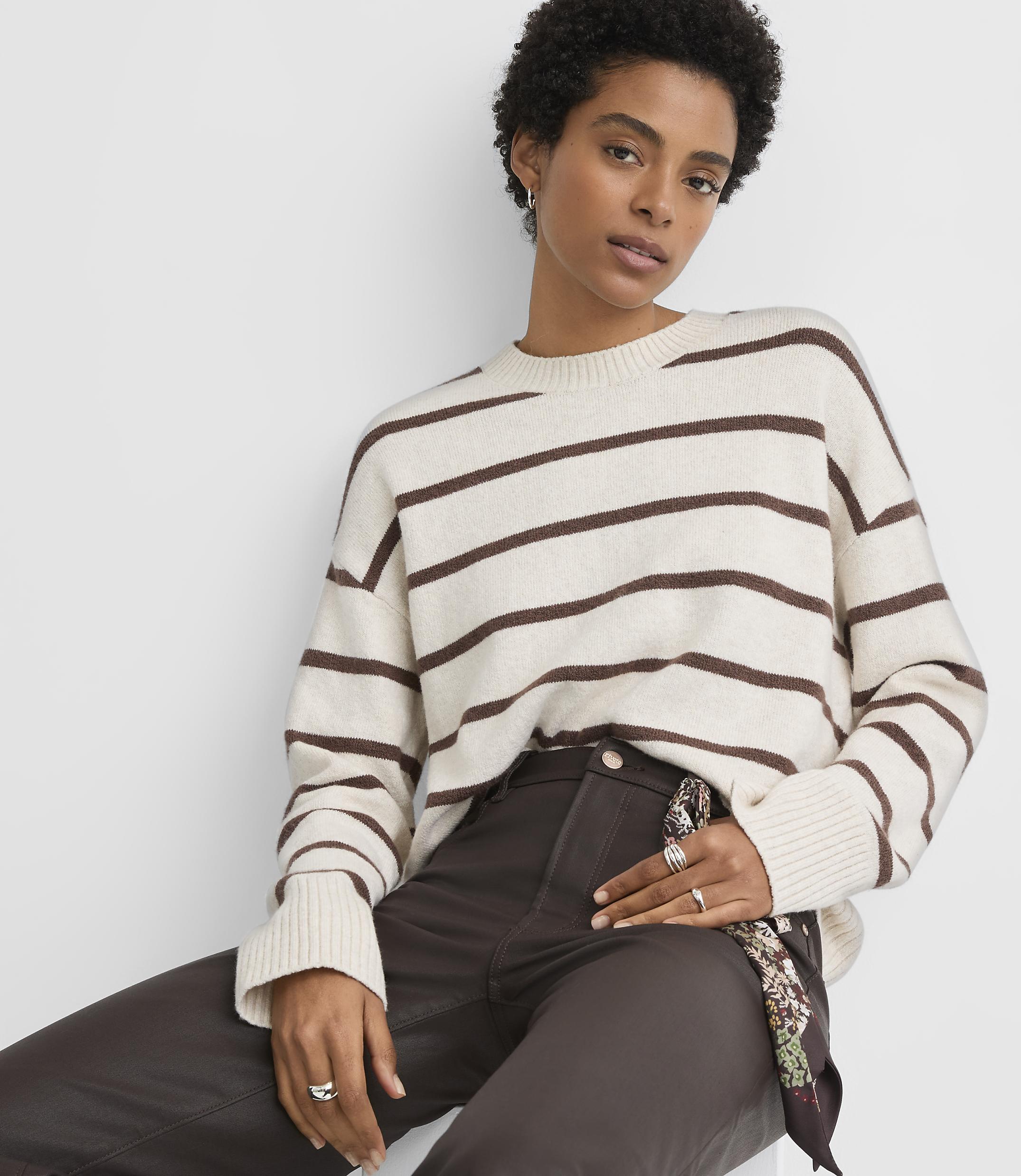 A woman in a striped sweater and dark pants poses against a plain white background.