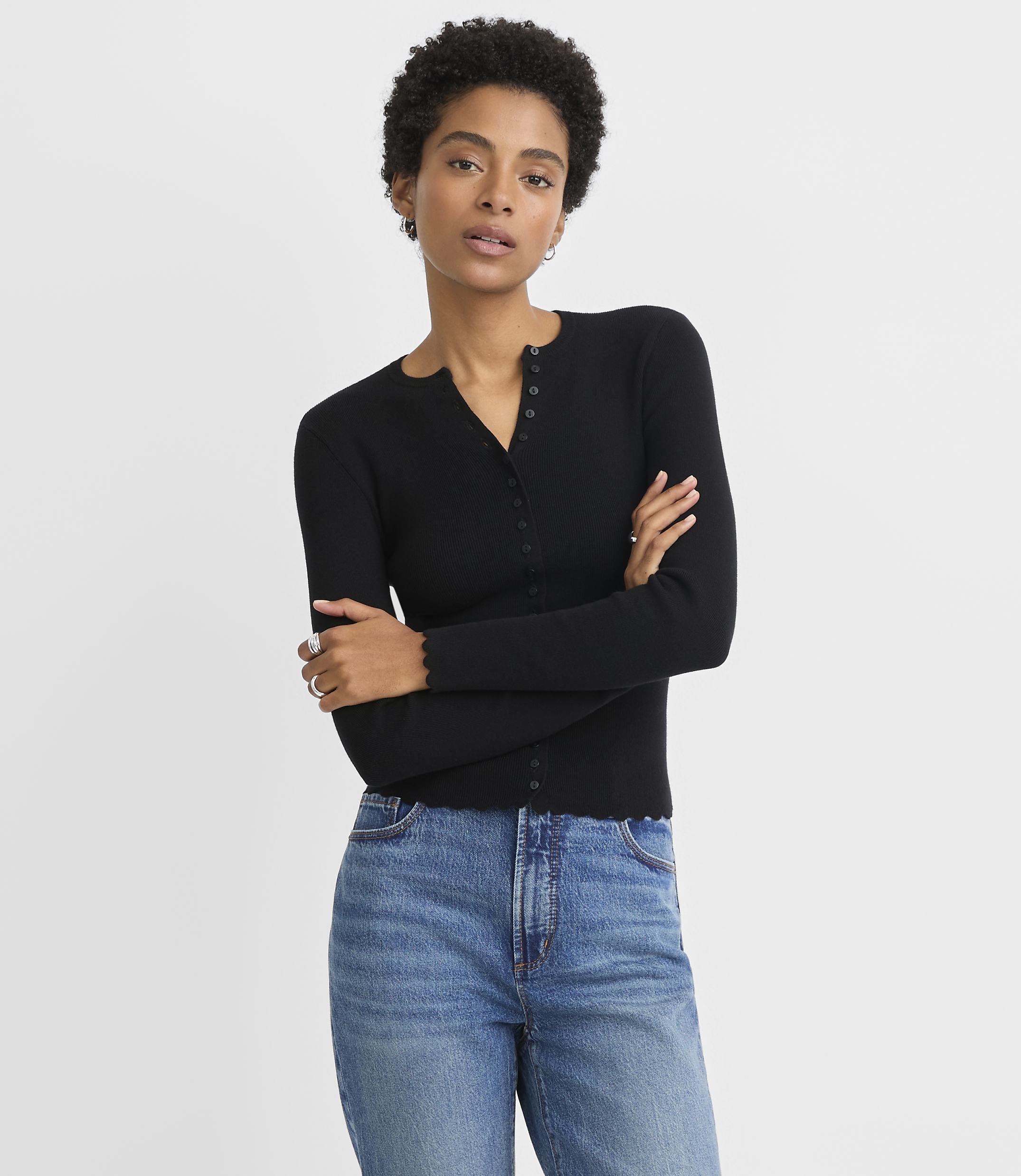 A woman in a black cardigan and blue jeans stands against a plain white background.