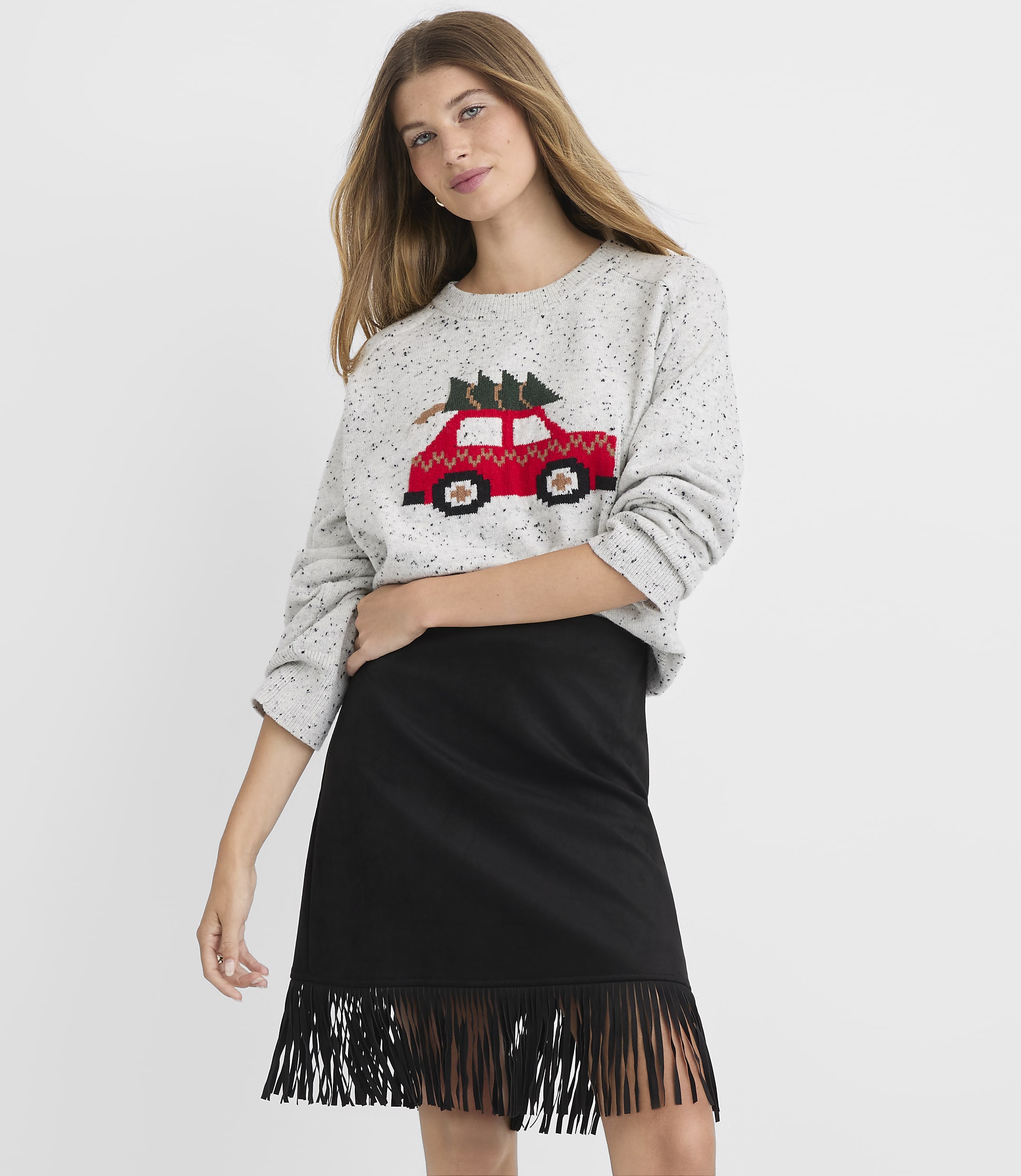 A woman in a grey sweater with a red car and Christmas tree design stands in front of a plain white background.