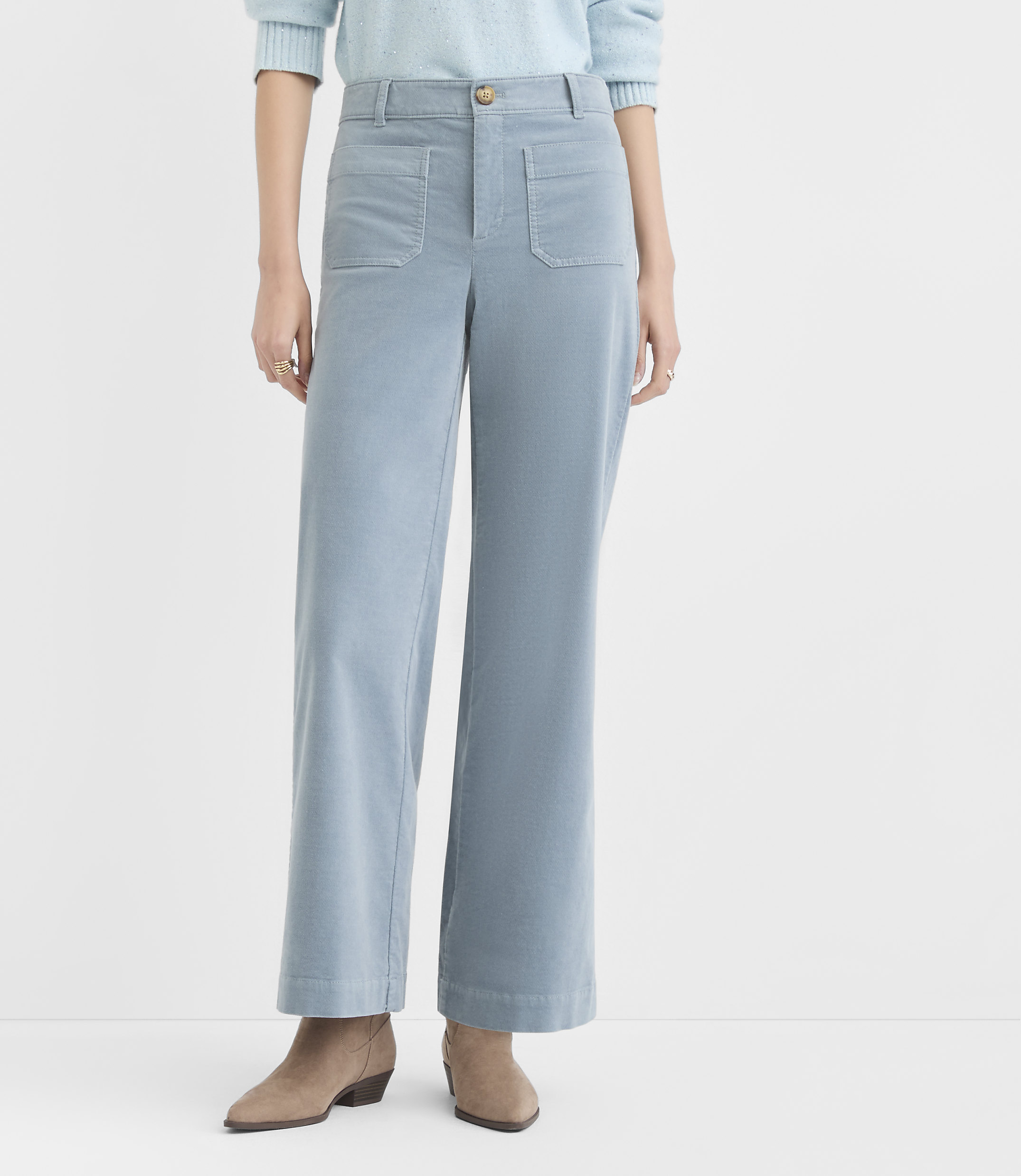 A person stands in light blue corduroy pants and tan ankle boots against a plain white background.