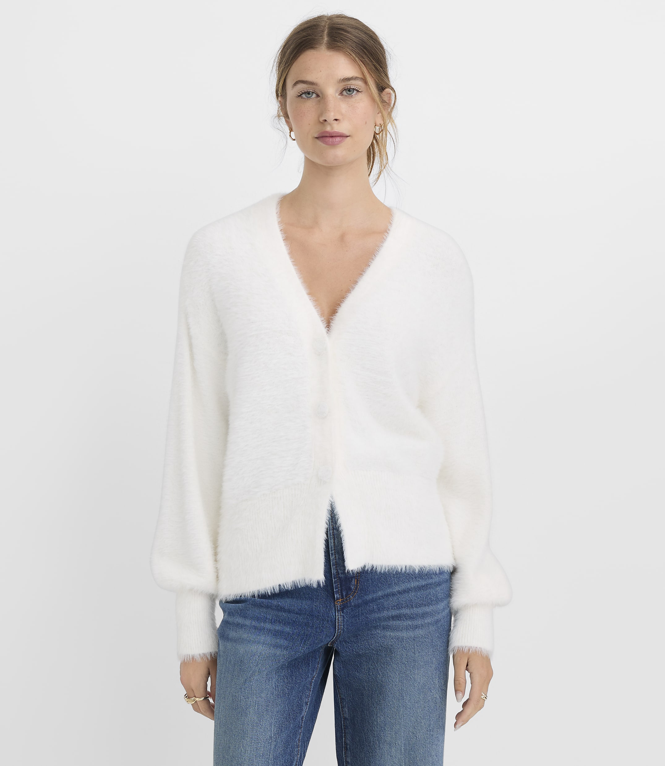 A woman in a fluffy white cardigan and blue jeans stands against a plain white background.