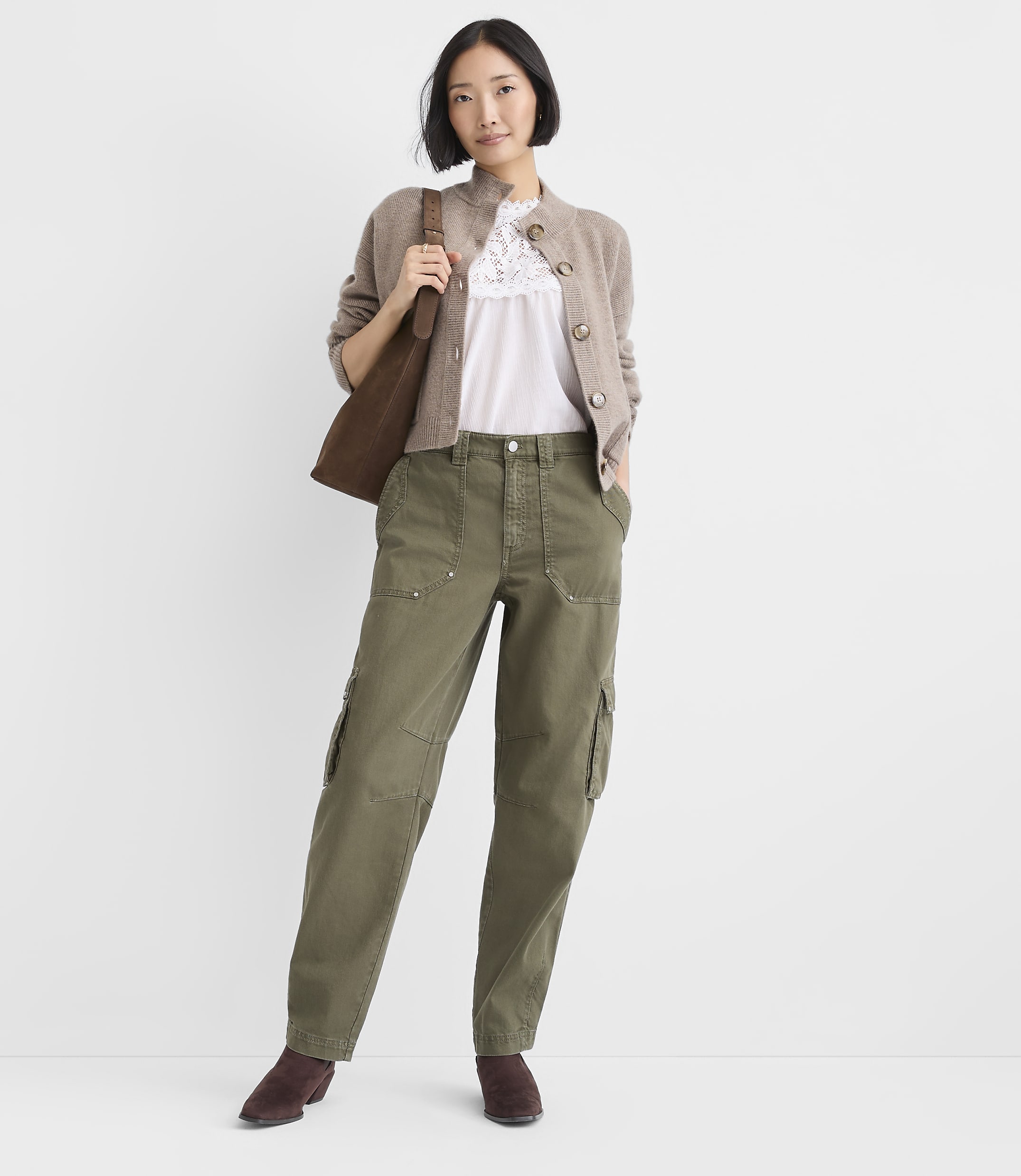 A woman wearing a beige cardigan, white lace top, and olive green cargo pants stands against a plain white background.