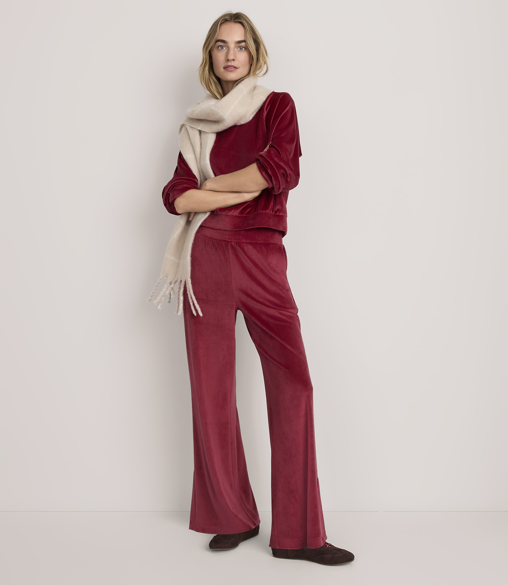 A woman wearing a red velvet two-piece outfit and a cream scarf stands against a plain white background.
