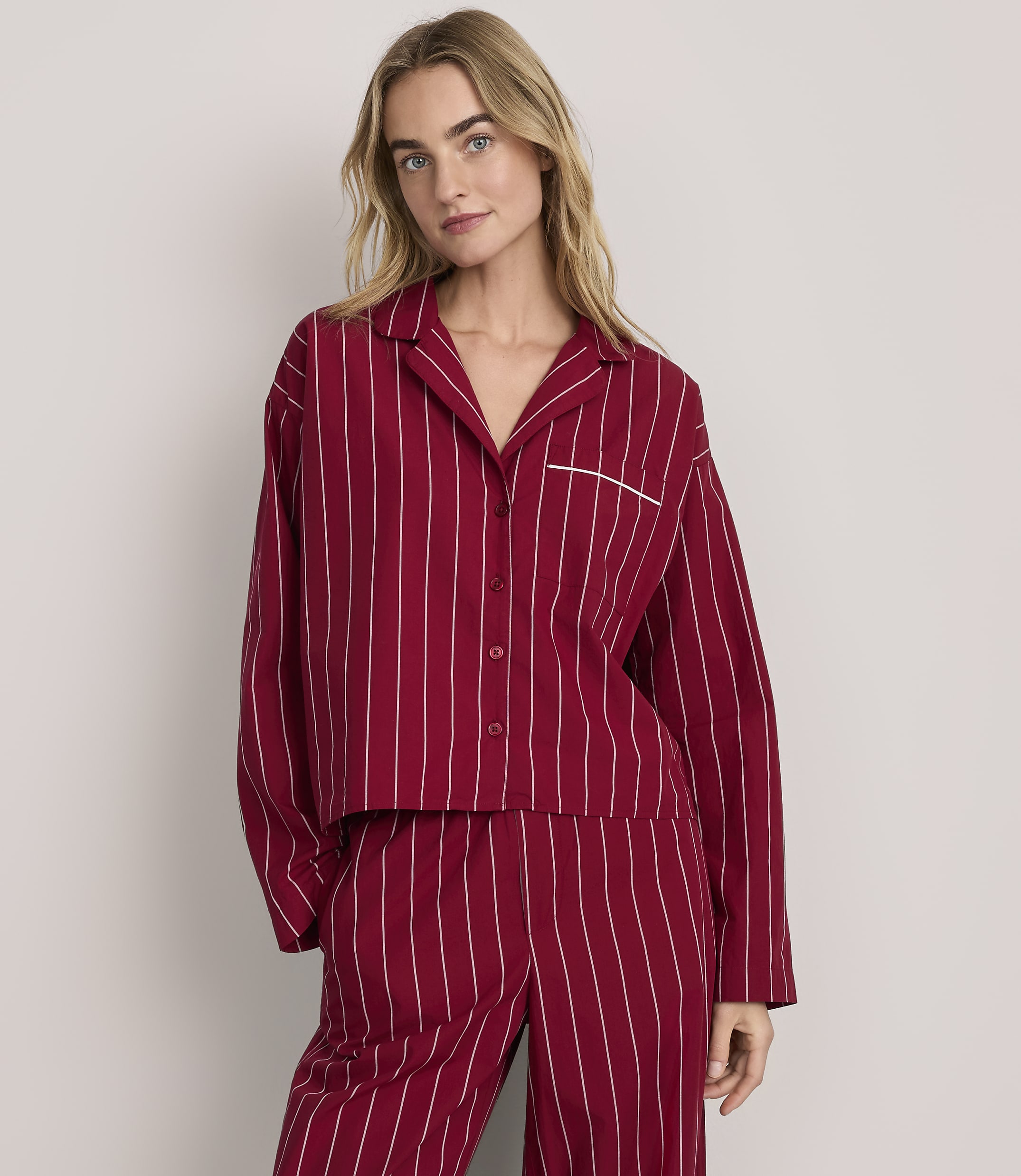 A woman wearing red and white striped pajamas stands against a plain, light-colored background.