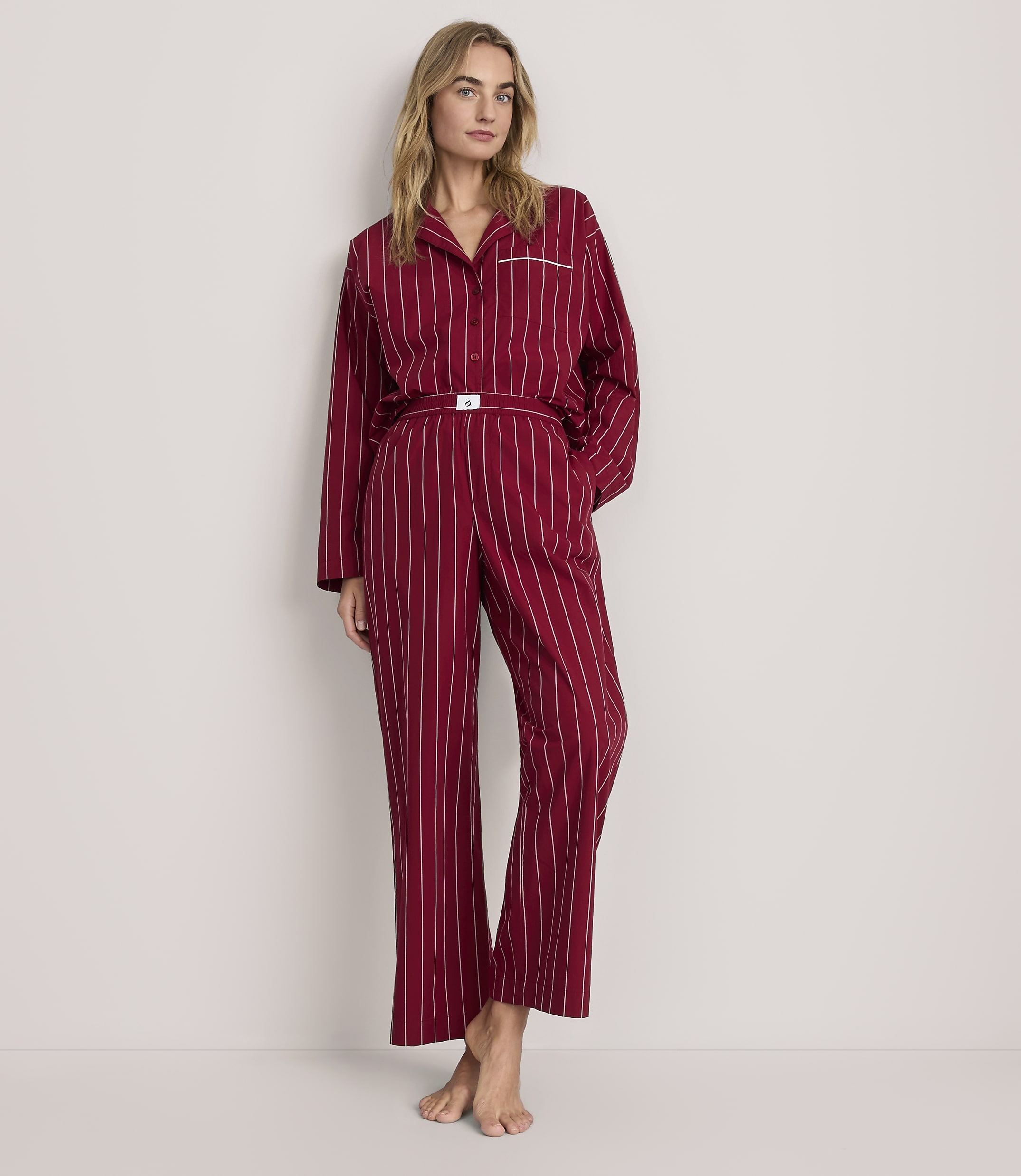 A woman wearing red striped pajamas stands against a plain, light-colored background.