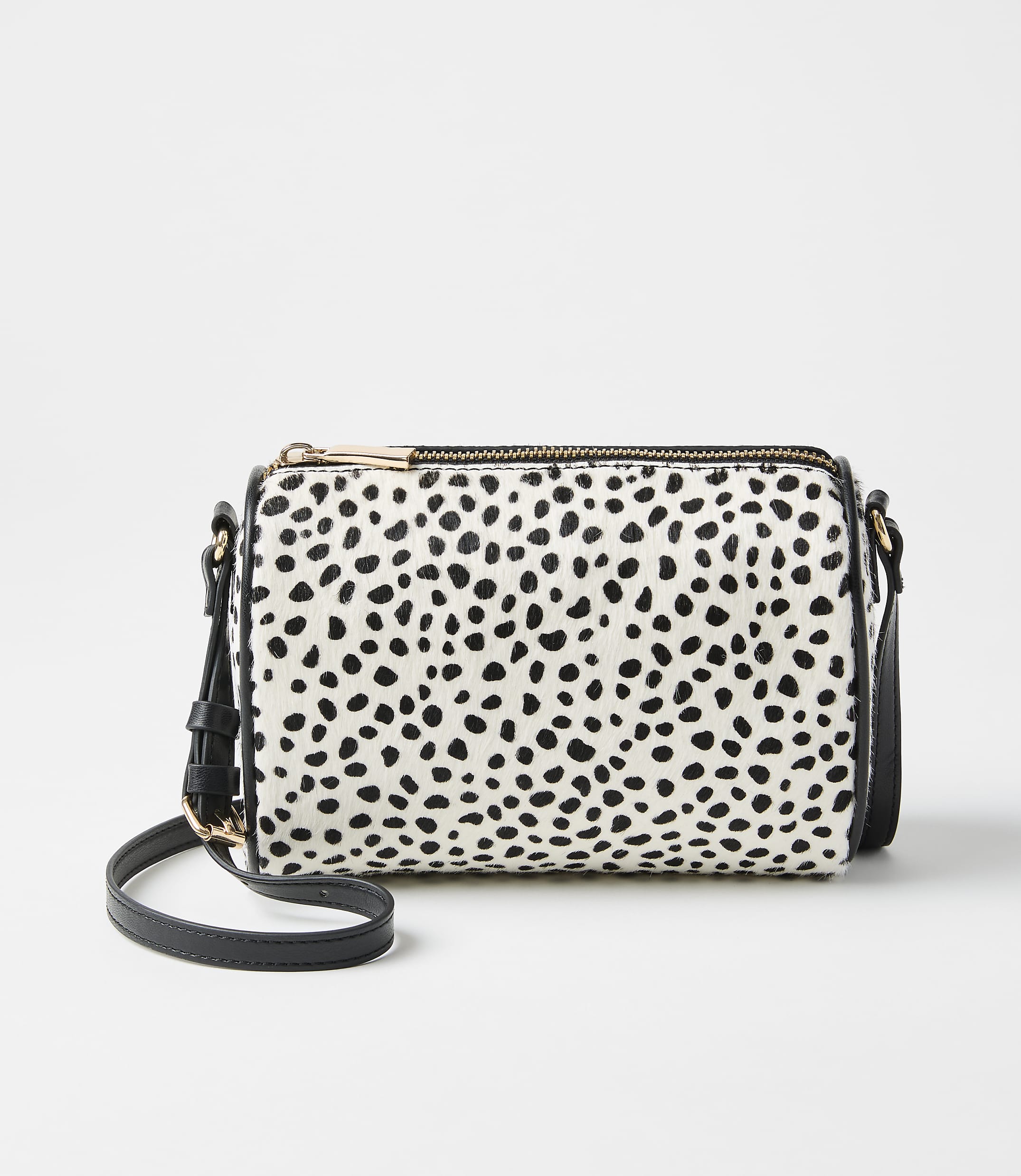 A white and black spotted handbag sits in the foreground against a plain, light gray background.