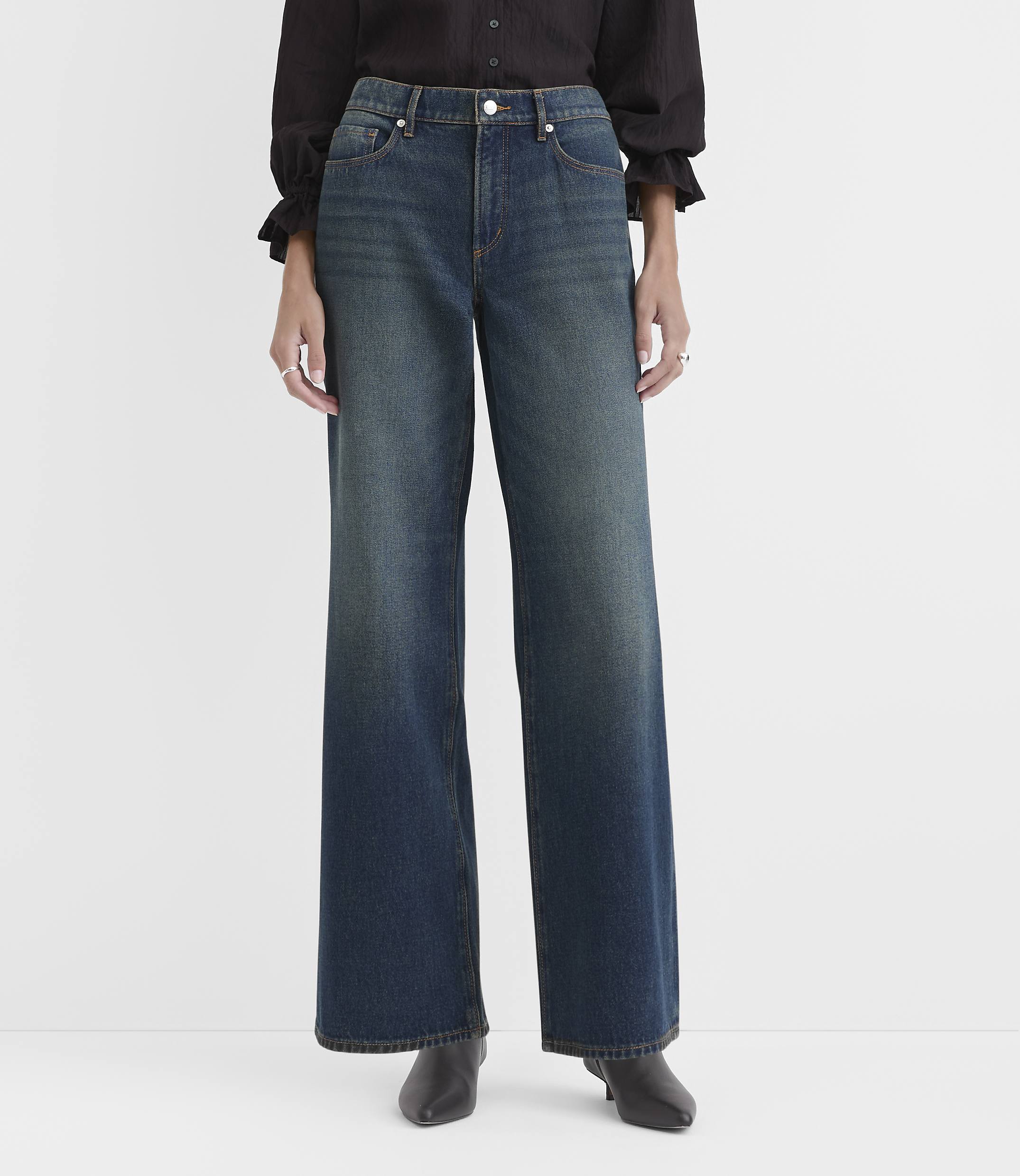 A person wearing a black blouse and wide-leg blue jeans stands against a plain white background.