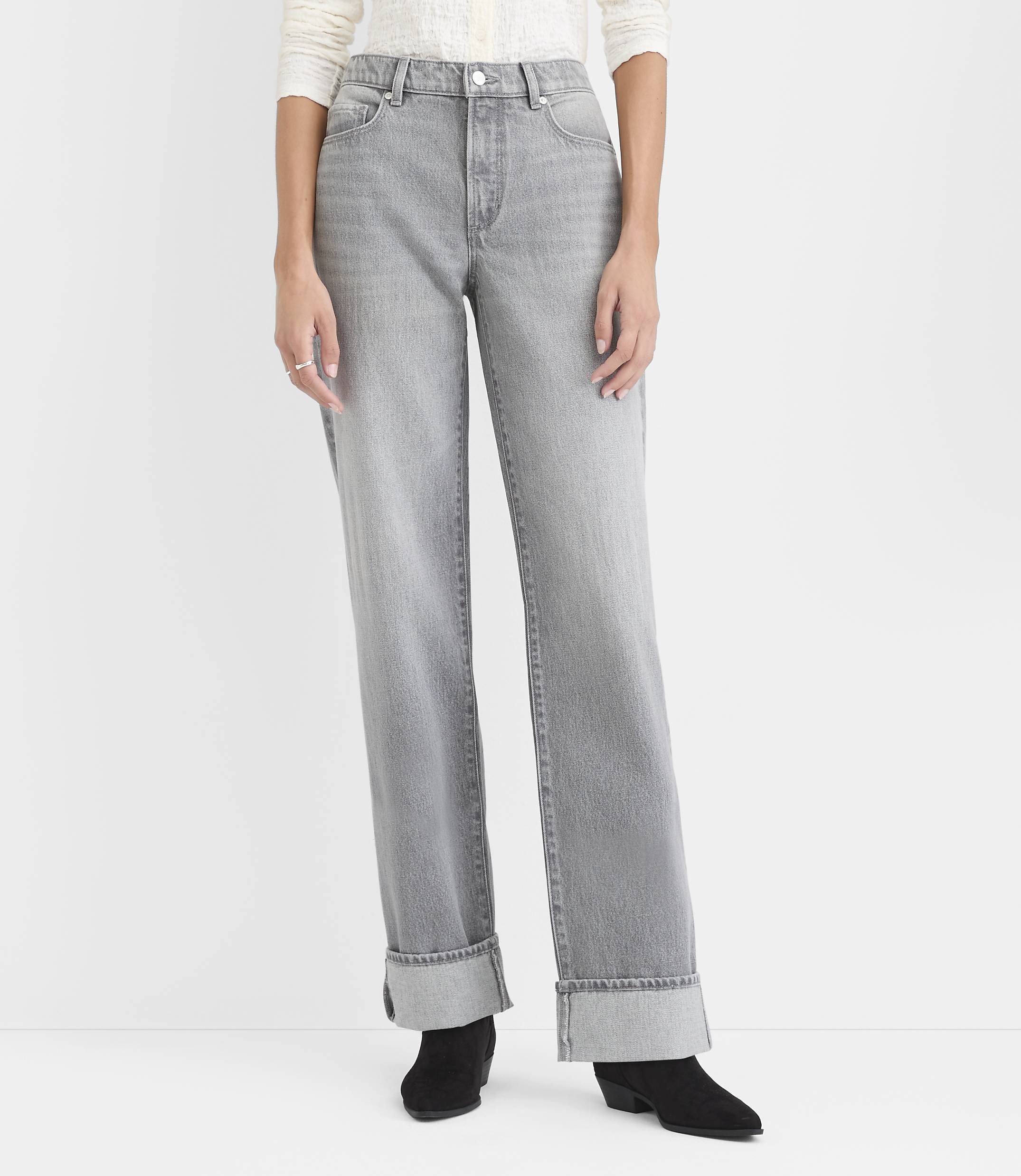 A person wearing a white top, wide-leg grey jeans, and black boots stands against a plain white background.
