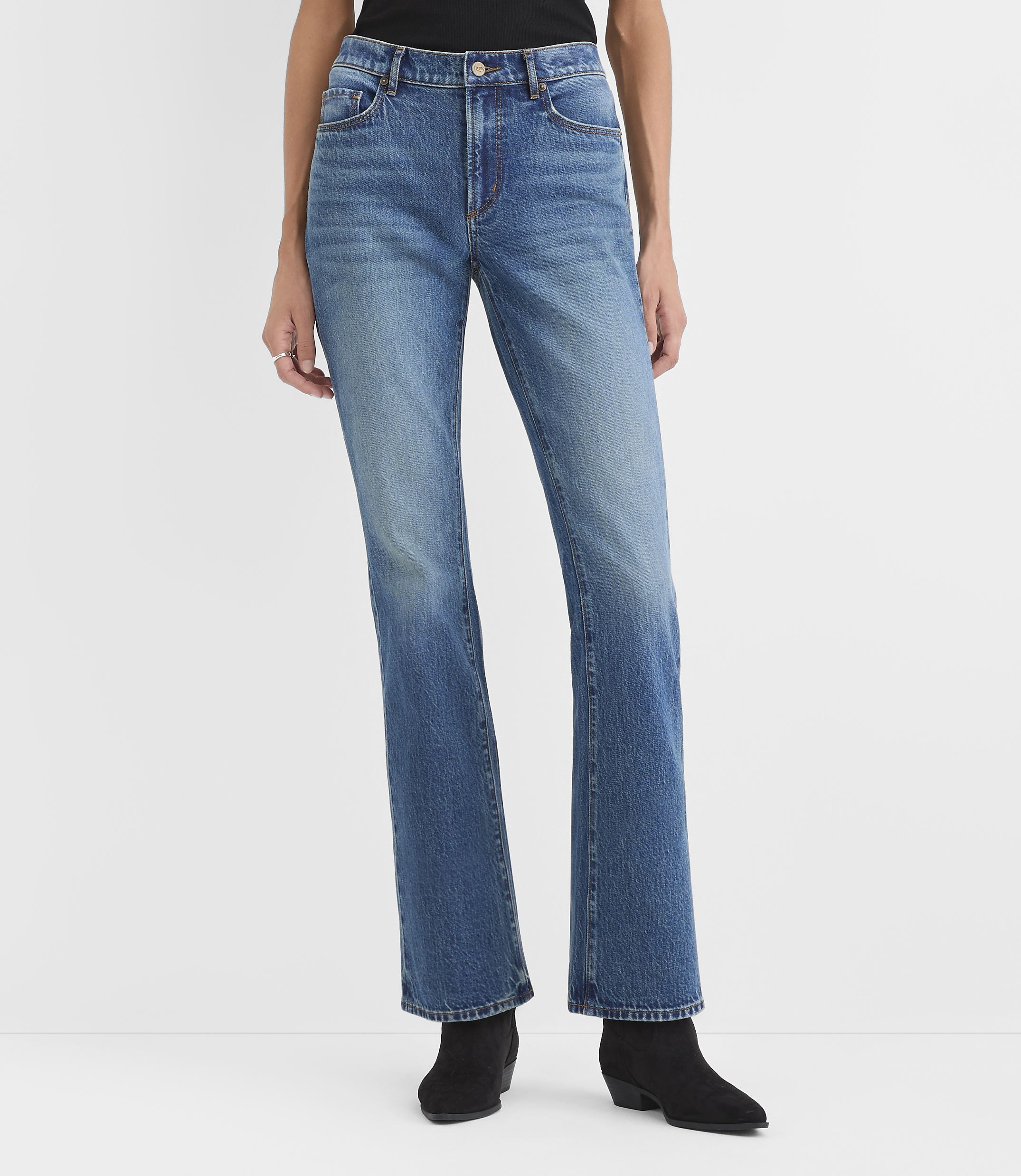 A person wearing blue jeans and black ankle boots stands against a plain white background.