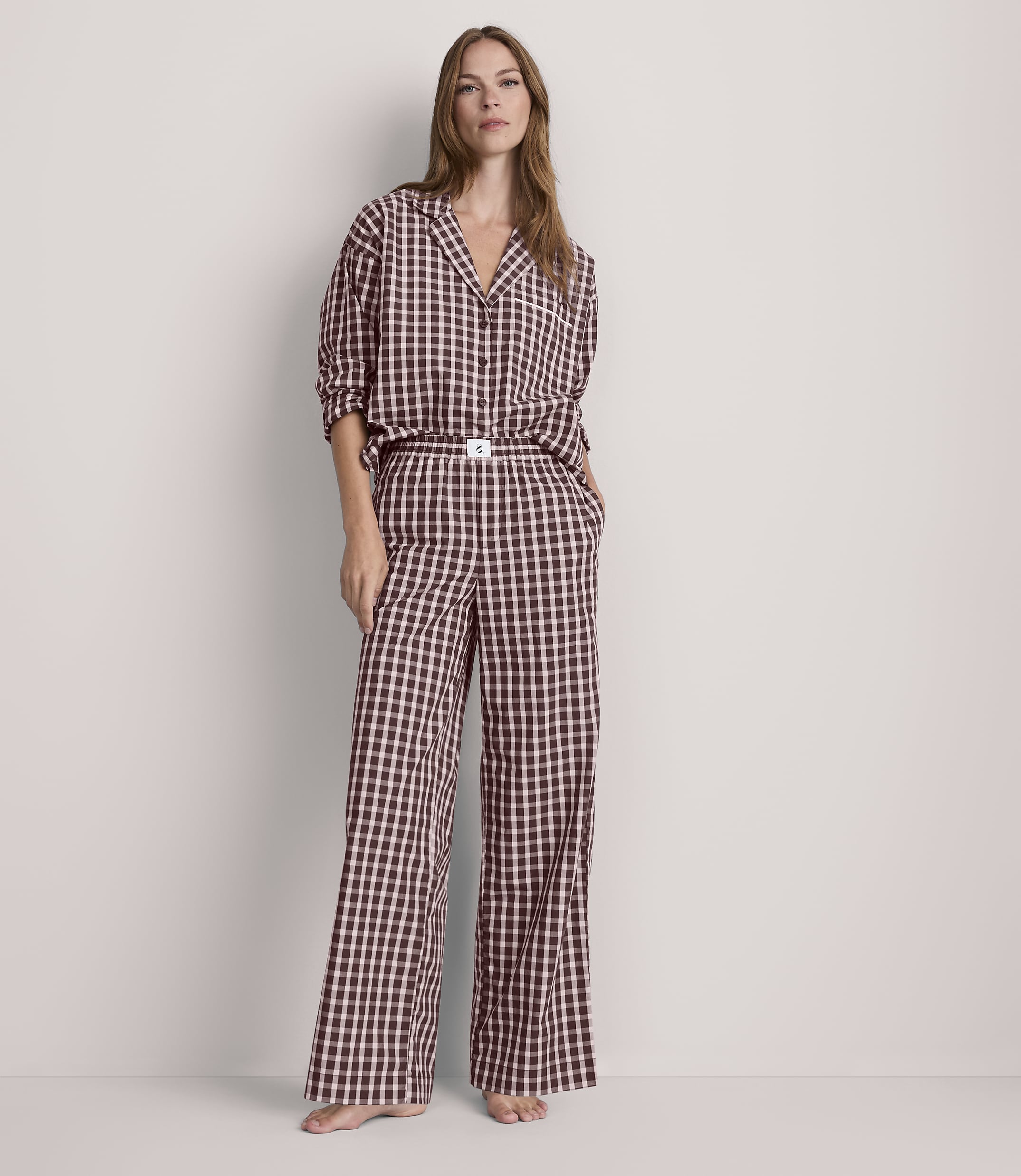 A woman stands in a light-colored room wearing a black and white checkered pajama set, with her hands in her pockets.