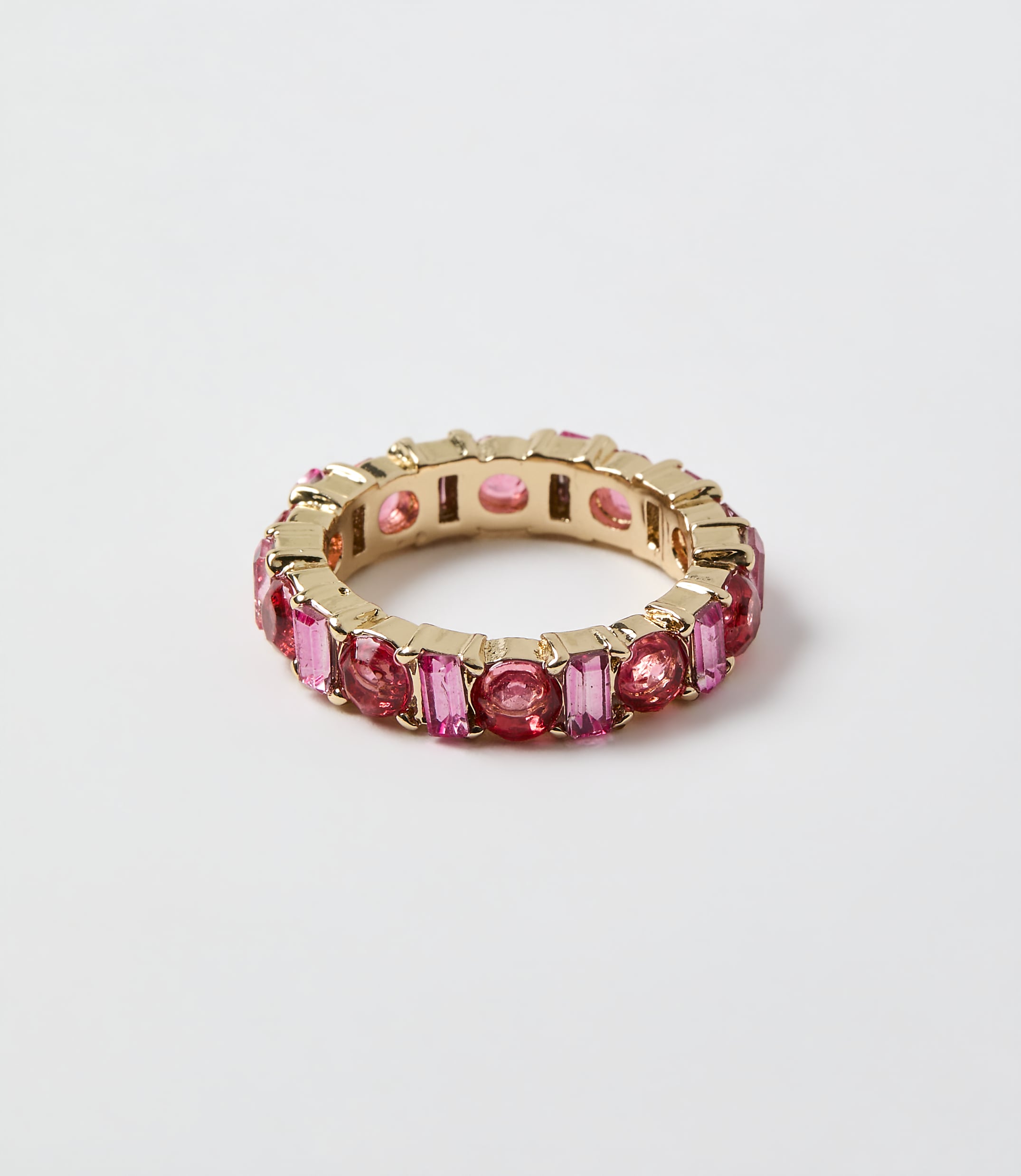 A gold ring set with pink gemstones rests on a plain white background.