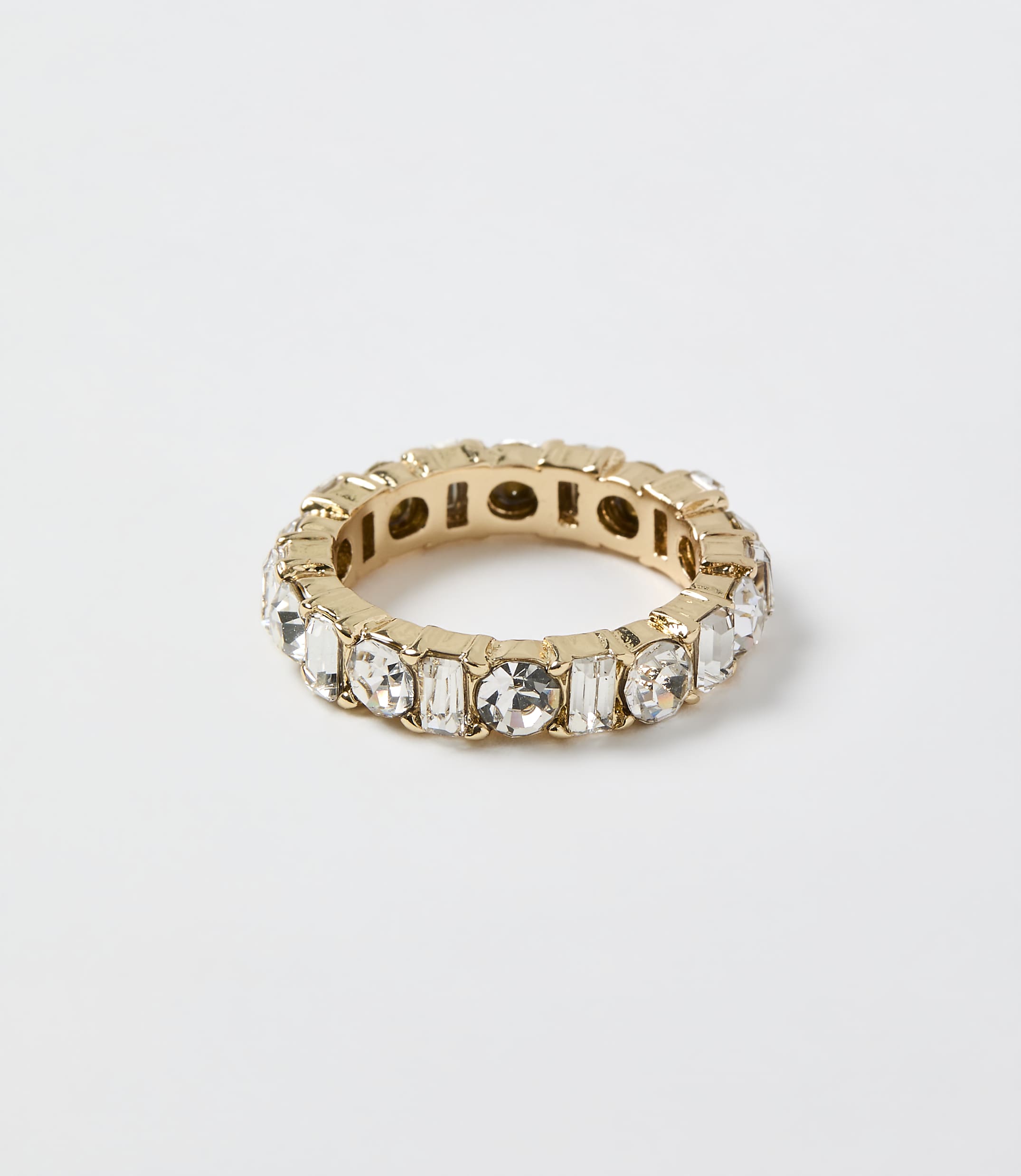 A gold ring set with clear crystals rests on a plain white background.