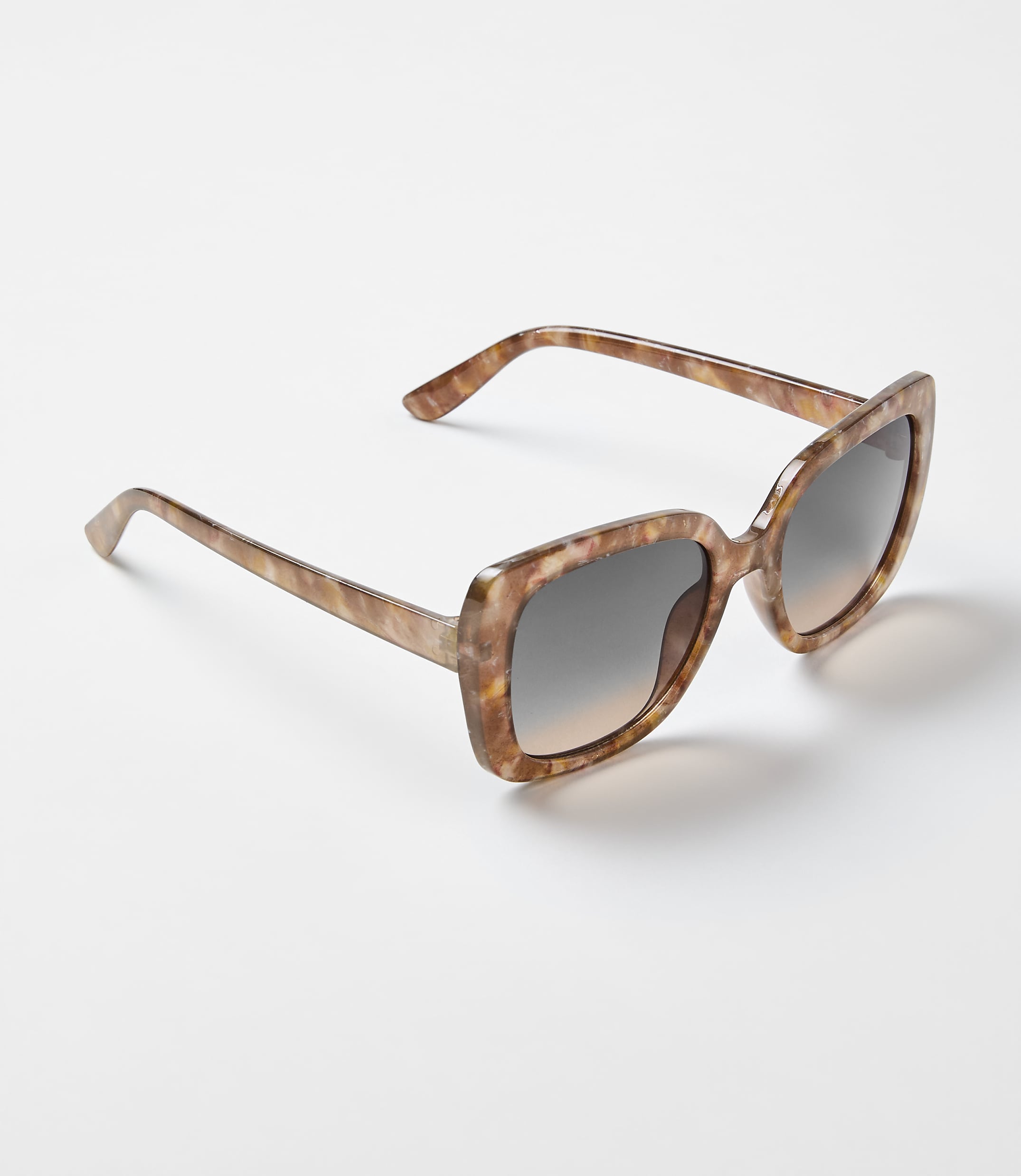 Brown tortoiseshell sunglasses rest on a plain, light-colored surface.