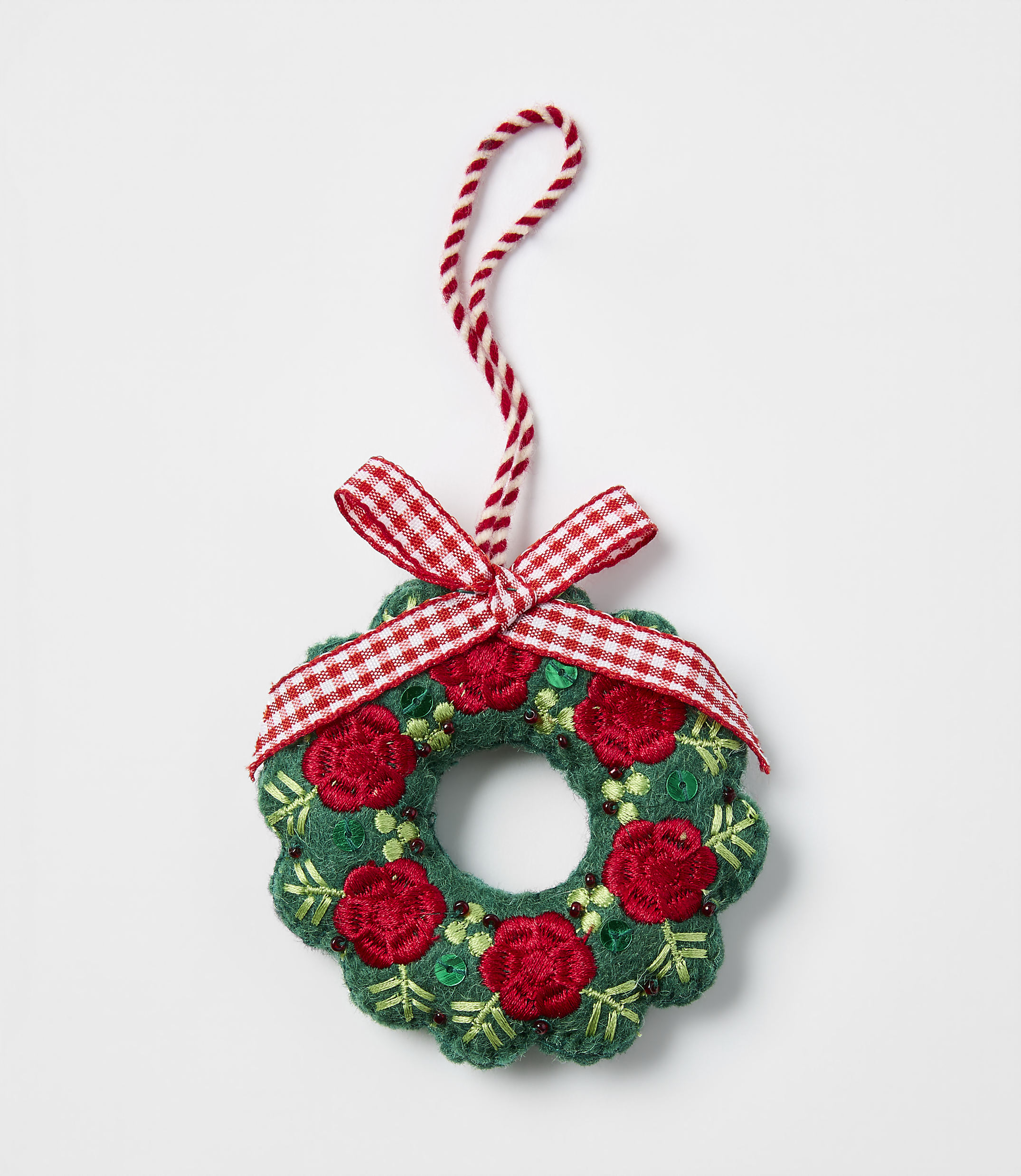 A small, handcrafted green wreath with red flowers and a red-and-white checkered bow rests against a plain white background.