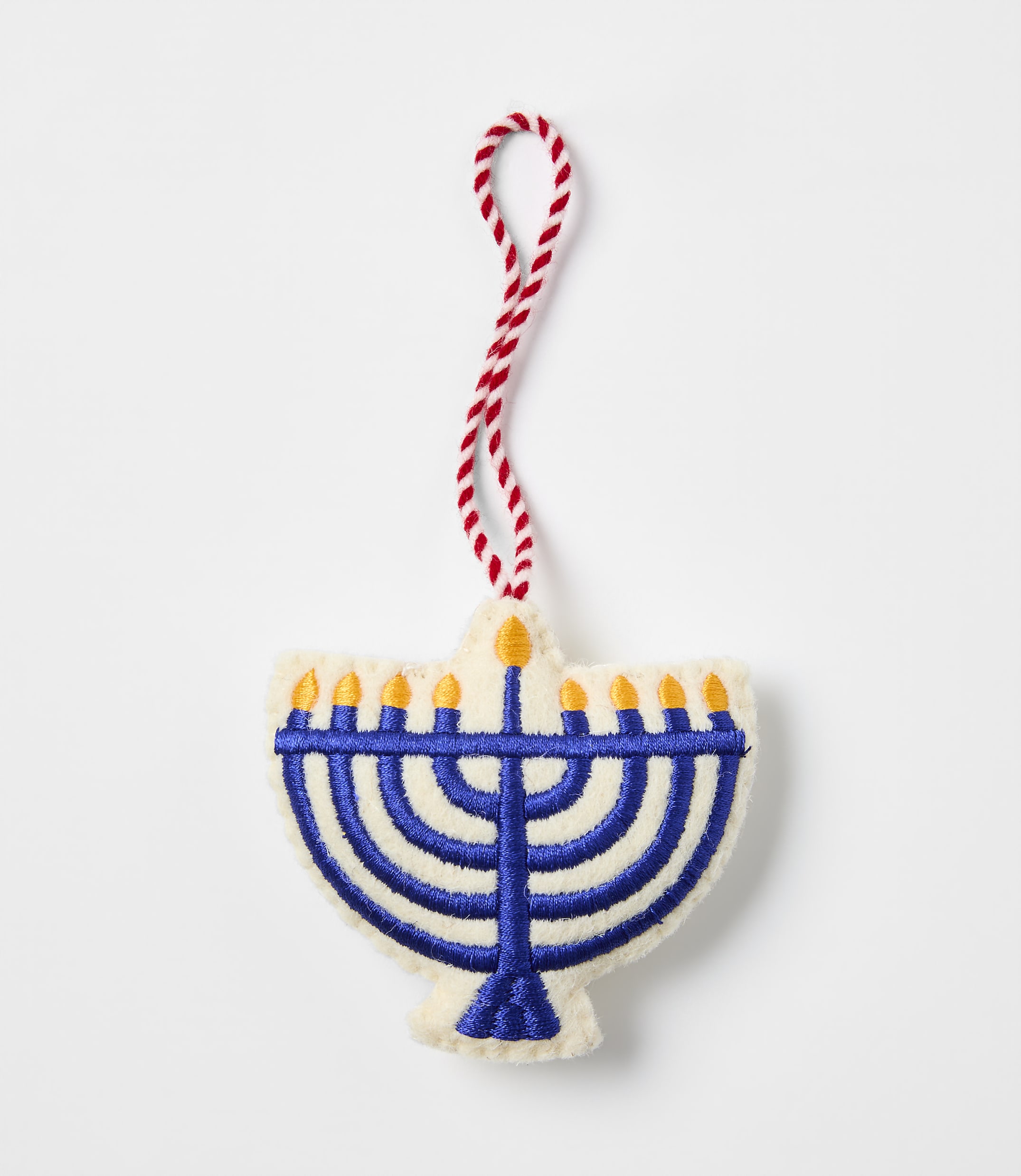 A blue embroidered menorah ornament with a red and white string hangs against a plain white background.