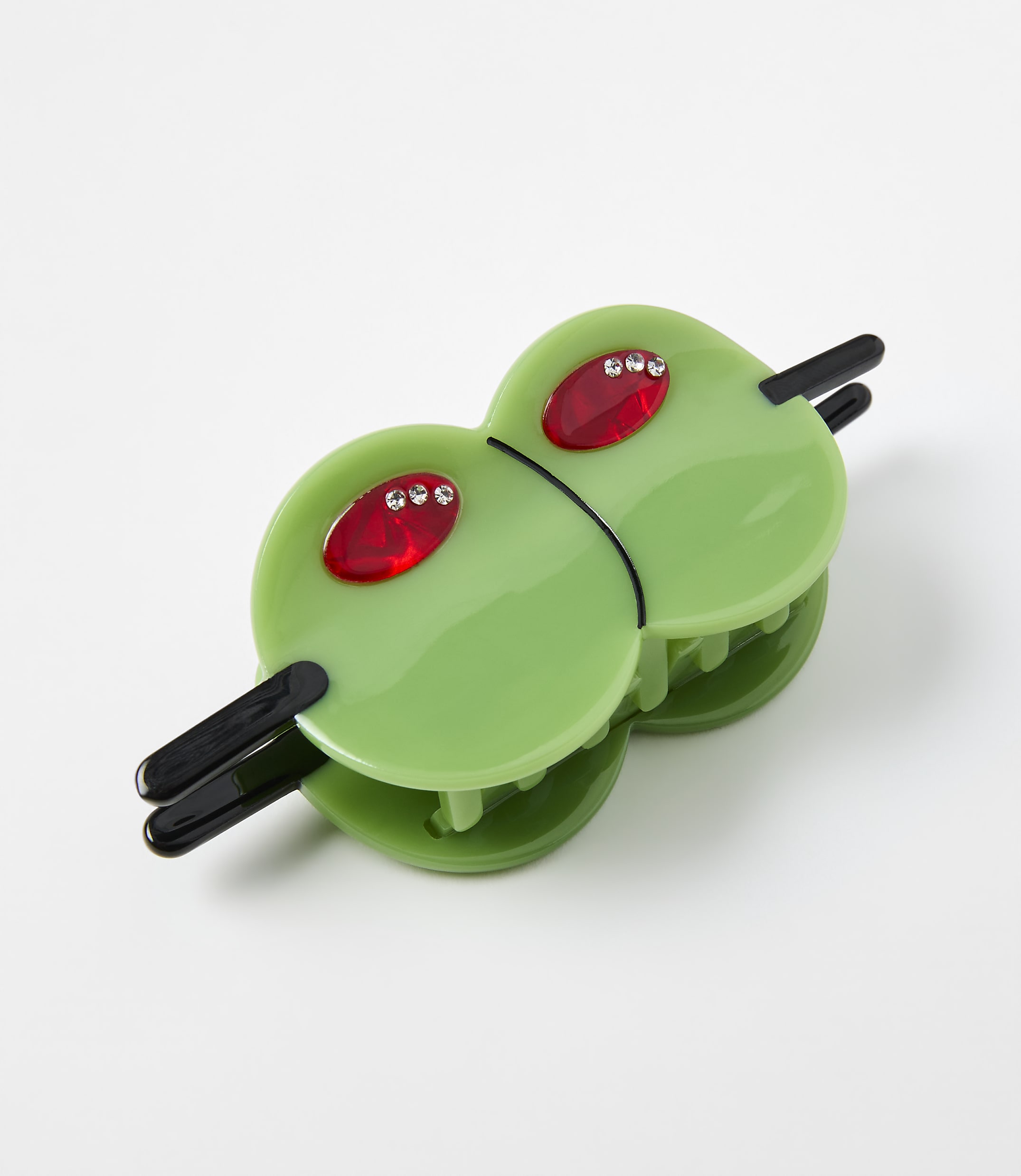 A green alien-shaped hair clip with red rhinestone eyes rests on a plain white background.