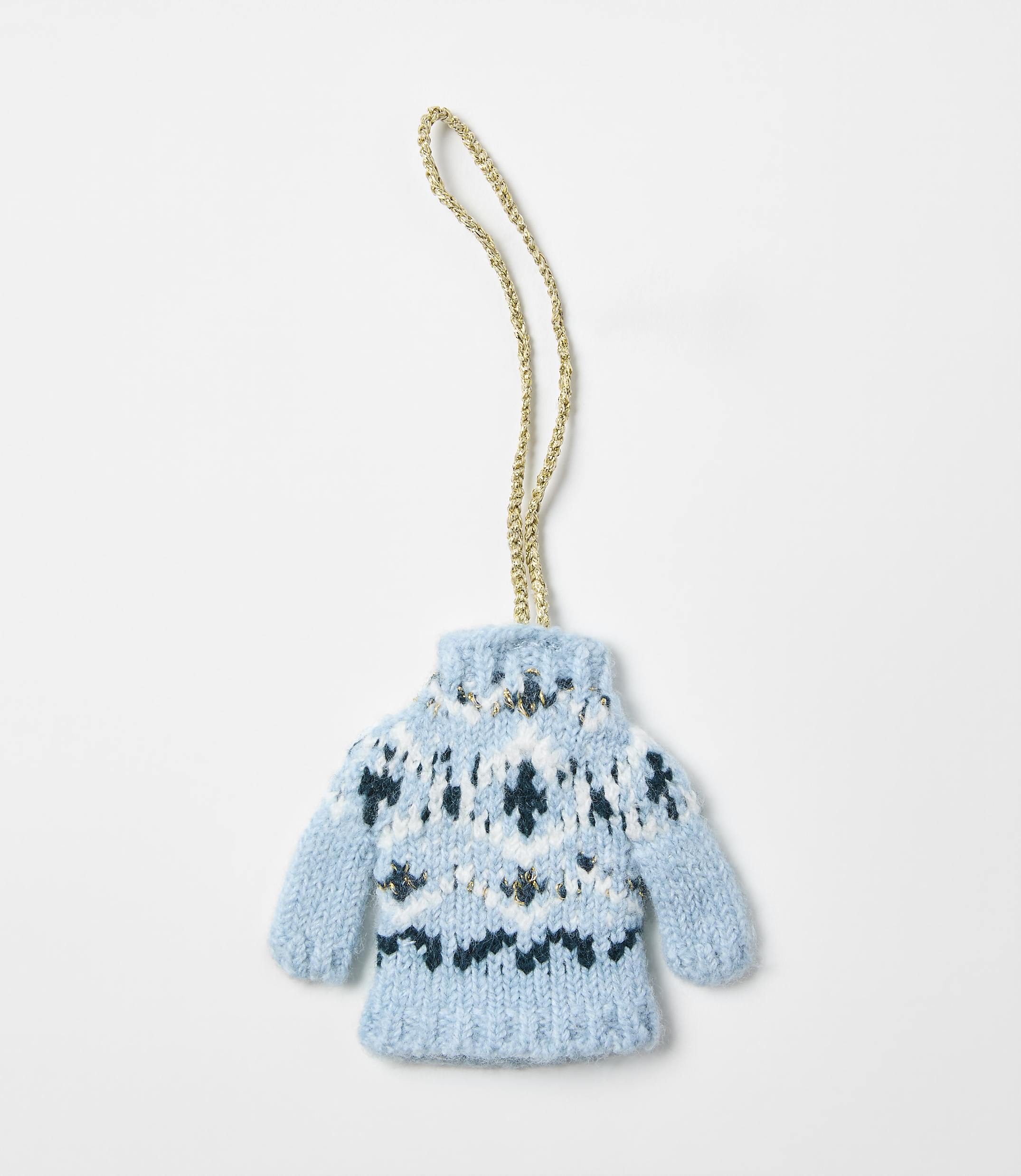 A small, blue knitted sweater ornament with a gold string hangs against a plain white background.