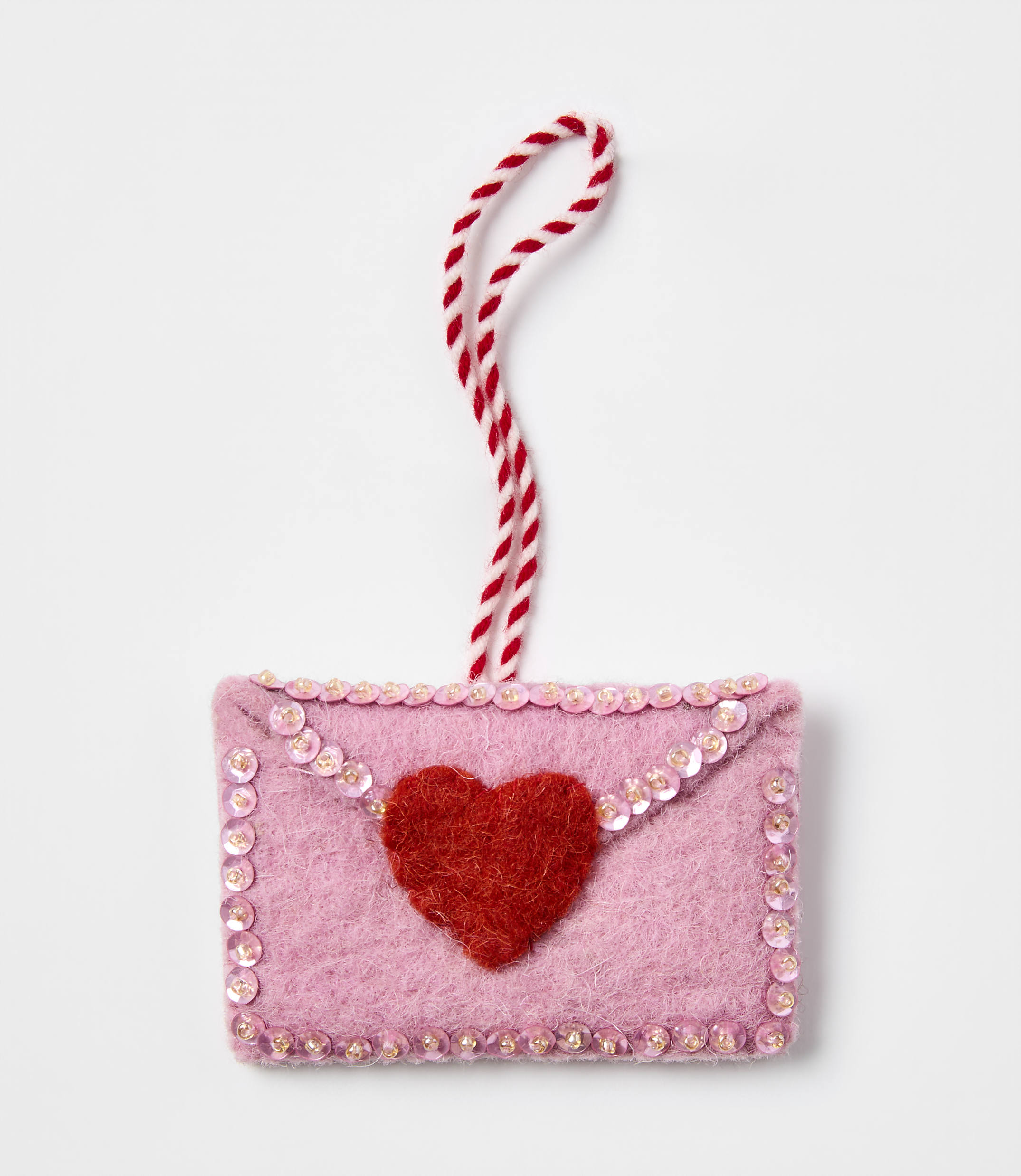 A pink felt envelope with a red heart and sequins sits against a plain white background.