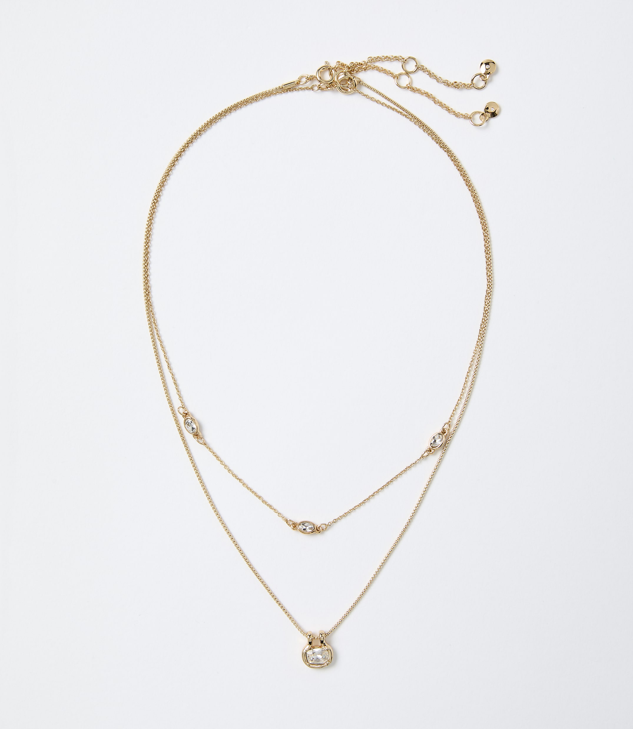A layered gold necklace with small sparkling crystals rests against a plain white background.