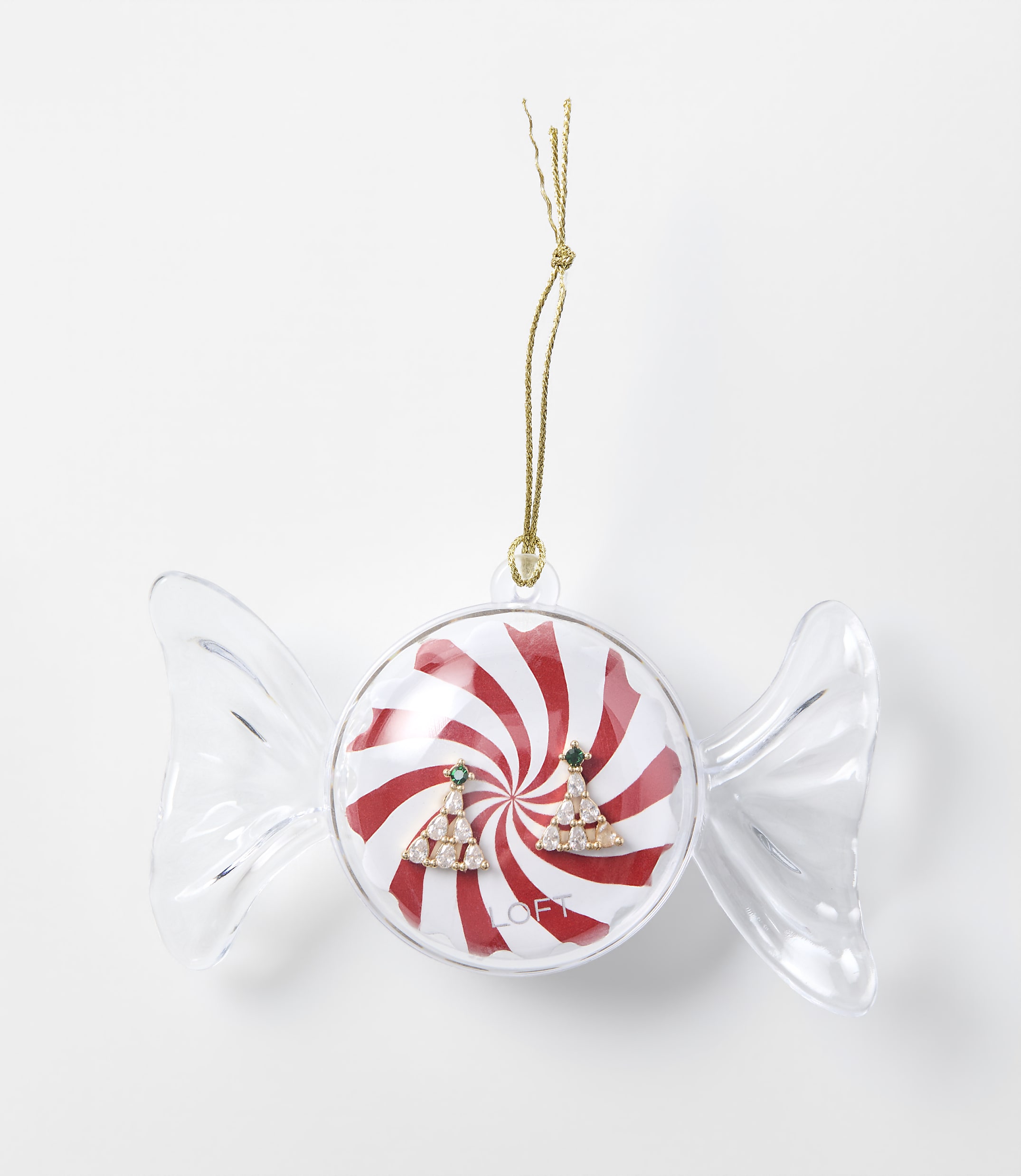 A pair of sparkling Christmas tree earrings sits inside a candy-shaped clear ornament with a red and white peppermint background, set against a plain white surface.