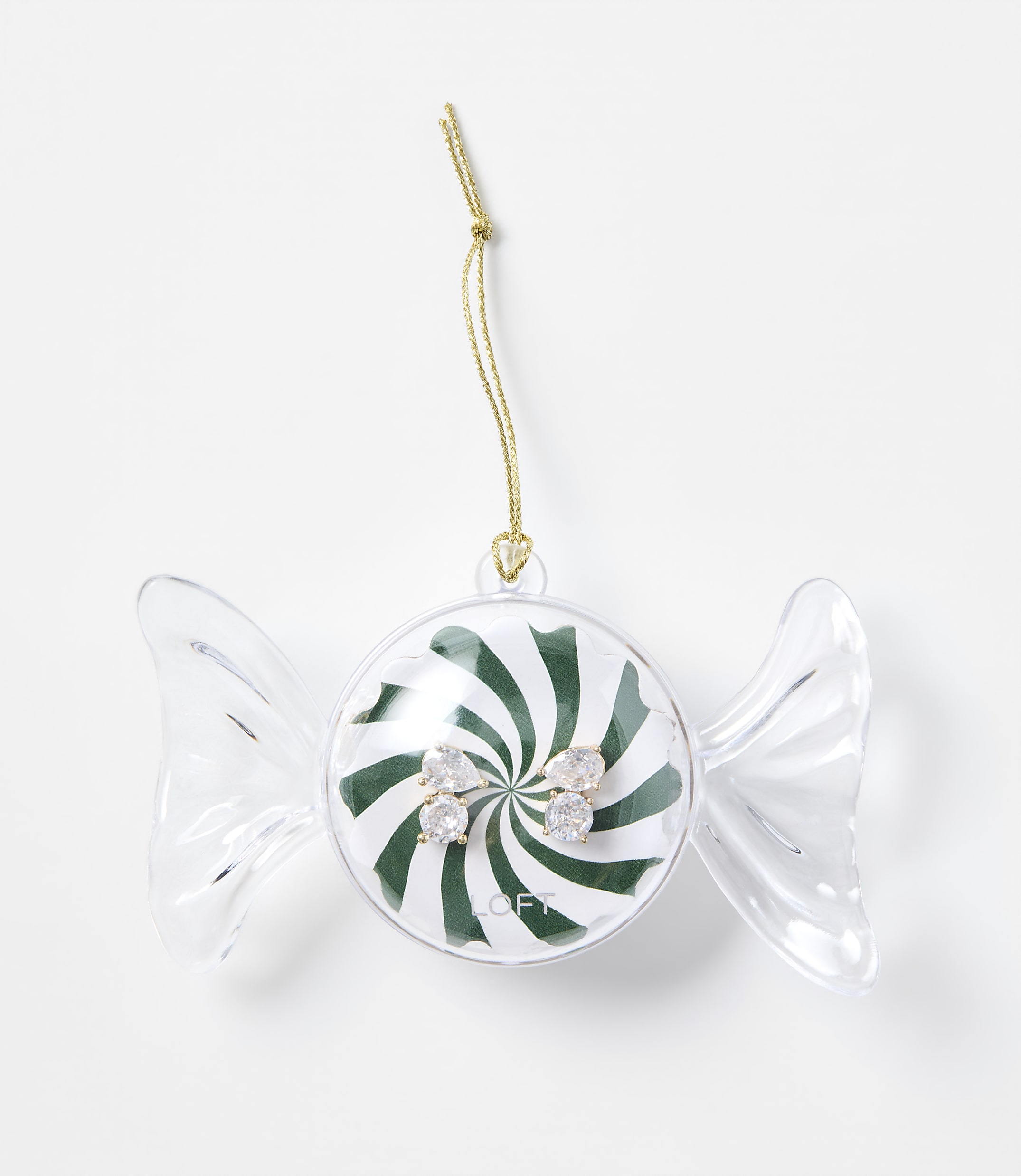 A pair of sparkling stud earrings sits inside a candy-shaped clear plastic ornament with a green and white swirl background, set against a plain white surface.