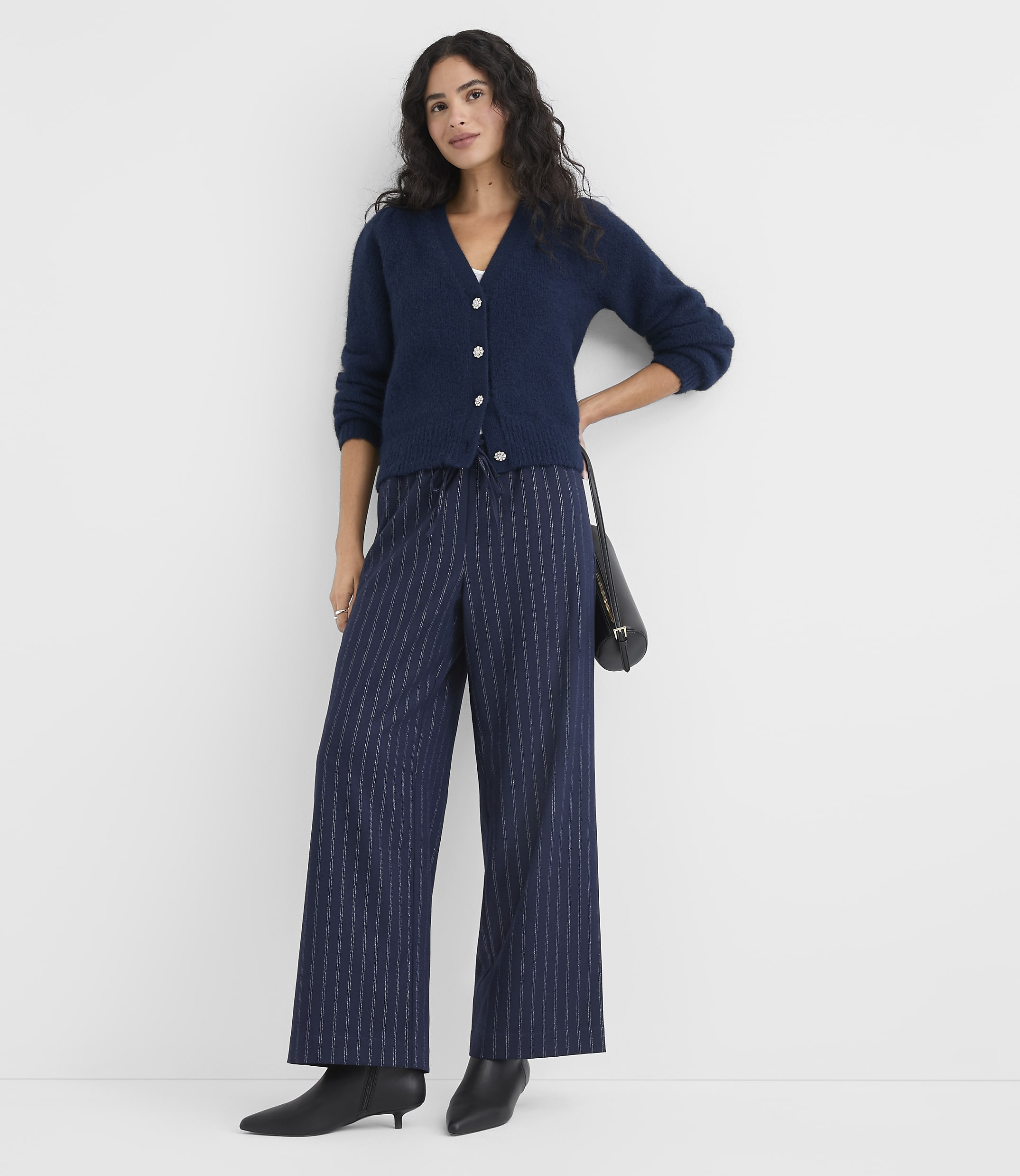 A woman wearing a navy blue cardigan and pinstriped wide-leg trousers stands against a plain white background.