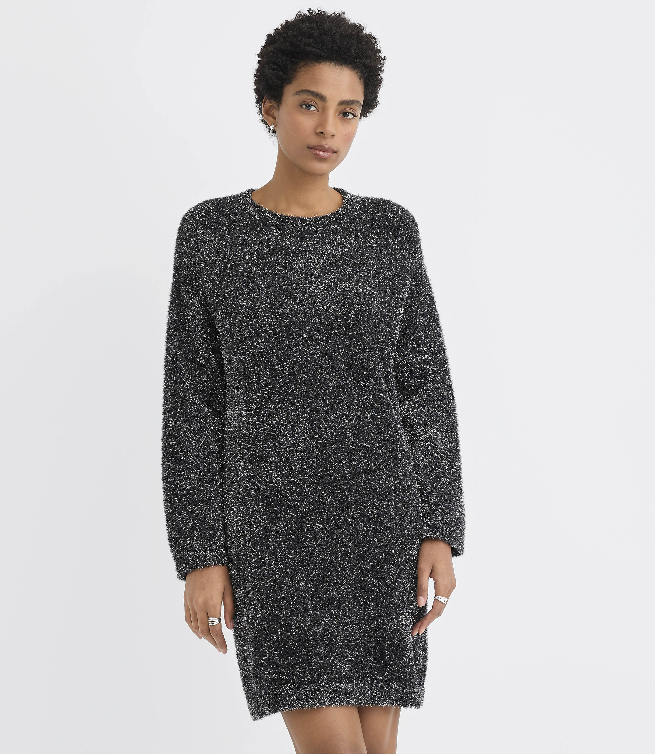 A woman wearing a shimmering dark grey knit dress stands against a plain white background.