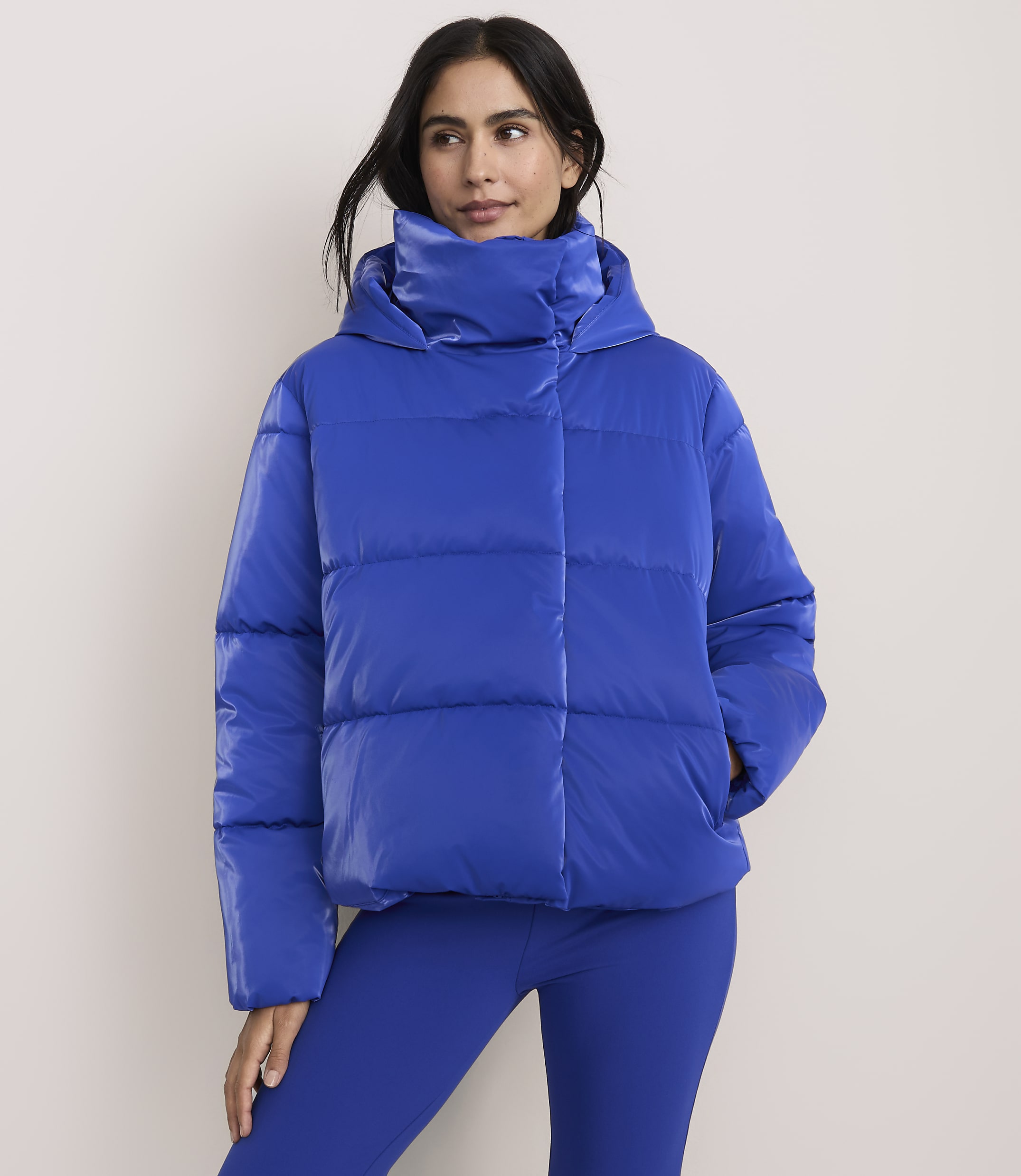 A woman wearing a bright blue puffer jacket and matching leggings stands against a plain, light-colored background.