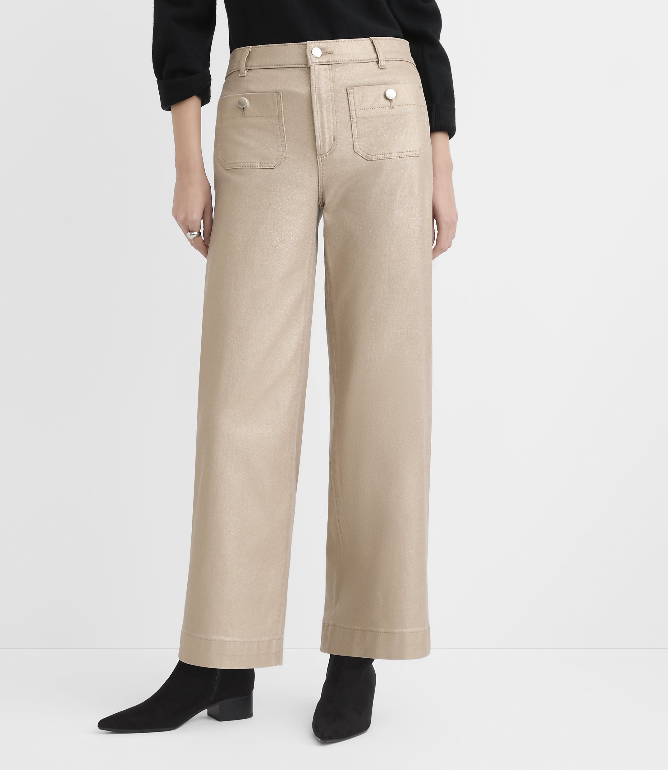 A person wearing a black top, wide-leg beige trousers, and black ankle boots stands against a plain white background.