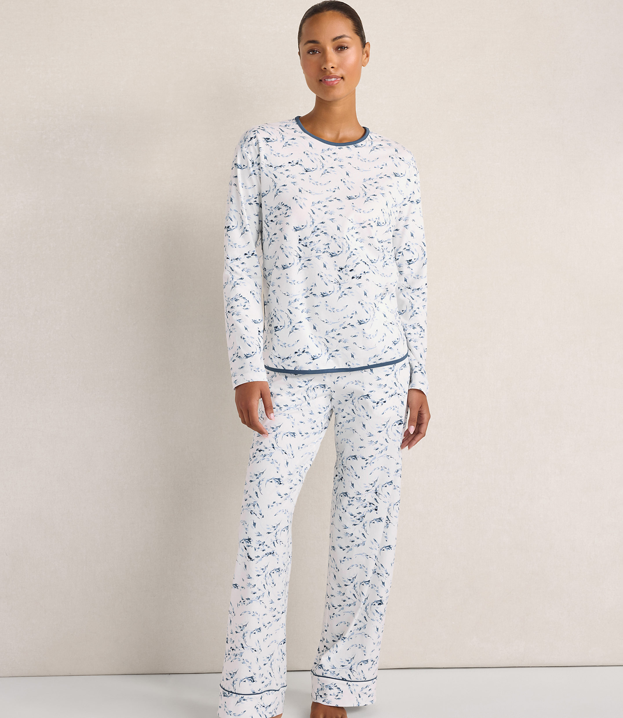 A woman wearing white and blue patterned pajamas stands against a plain, light-colored wall.