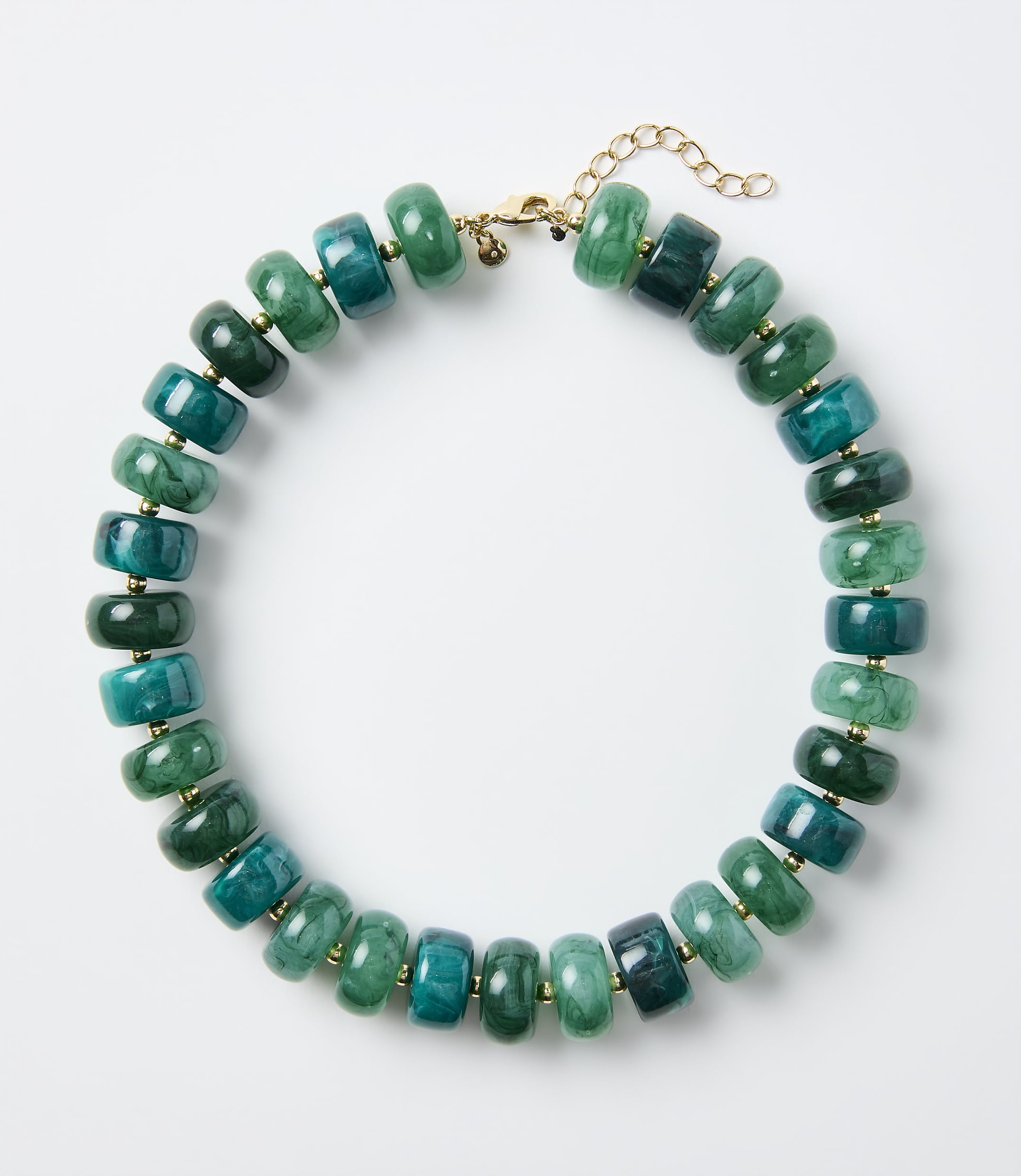 A necklace of green and teal stone beads rests on a plain white background.